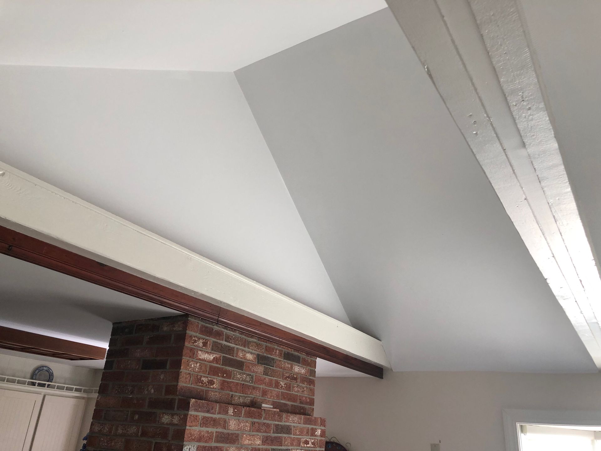 White vaulted ceiling with exposed wooden beams, a brick chimney, and painted walls.