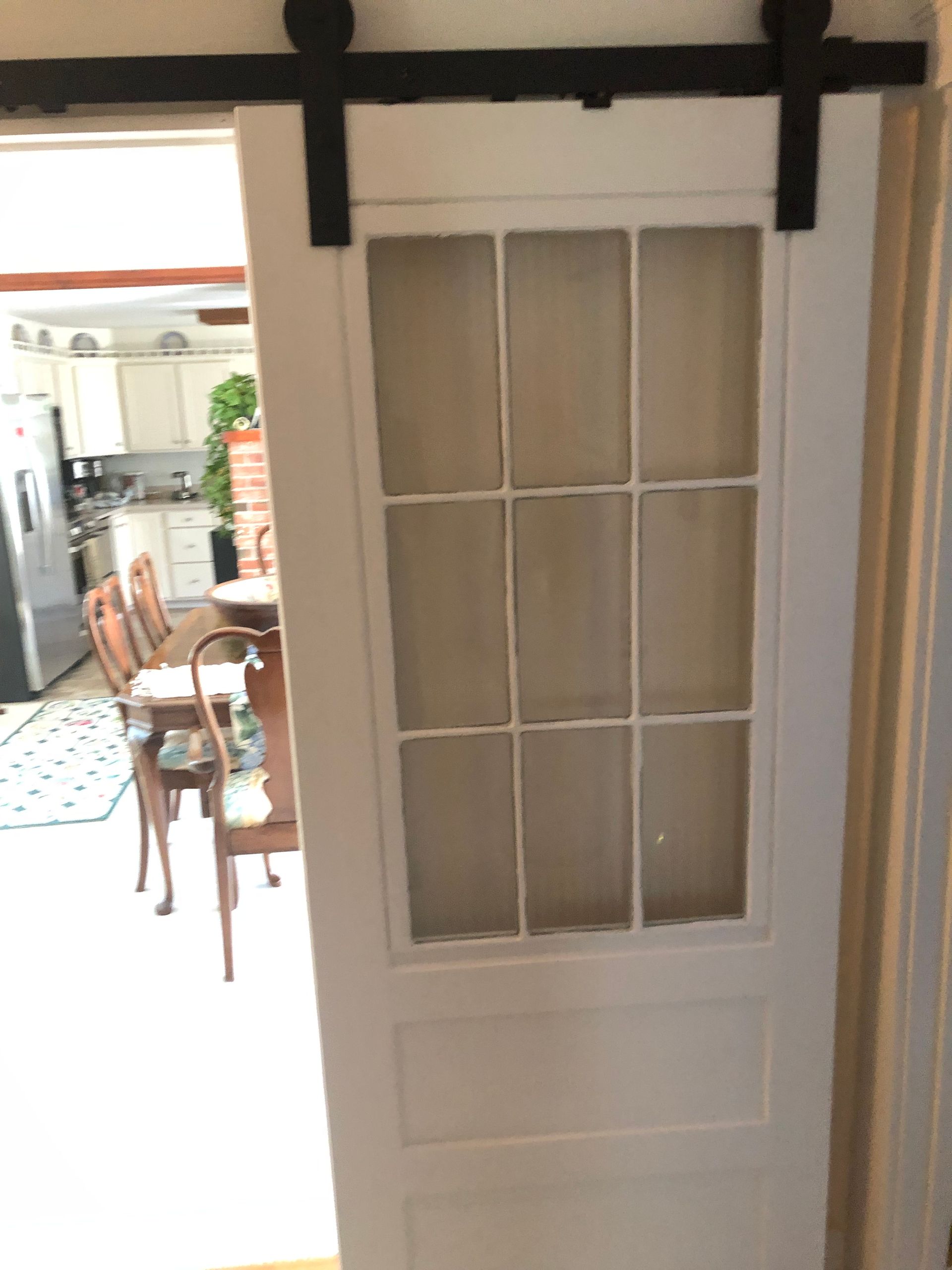 White paneled sliding door with glass panes, black track, and open view into a dining area.