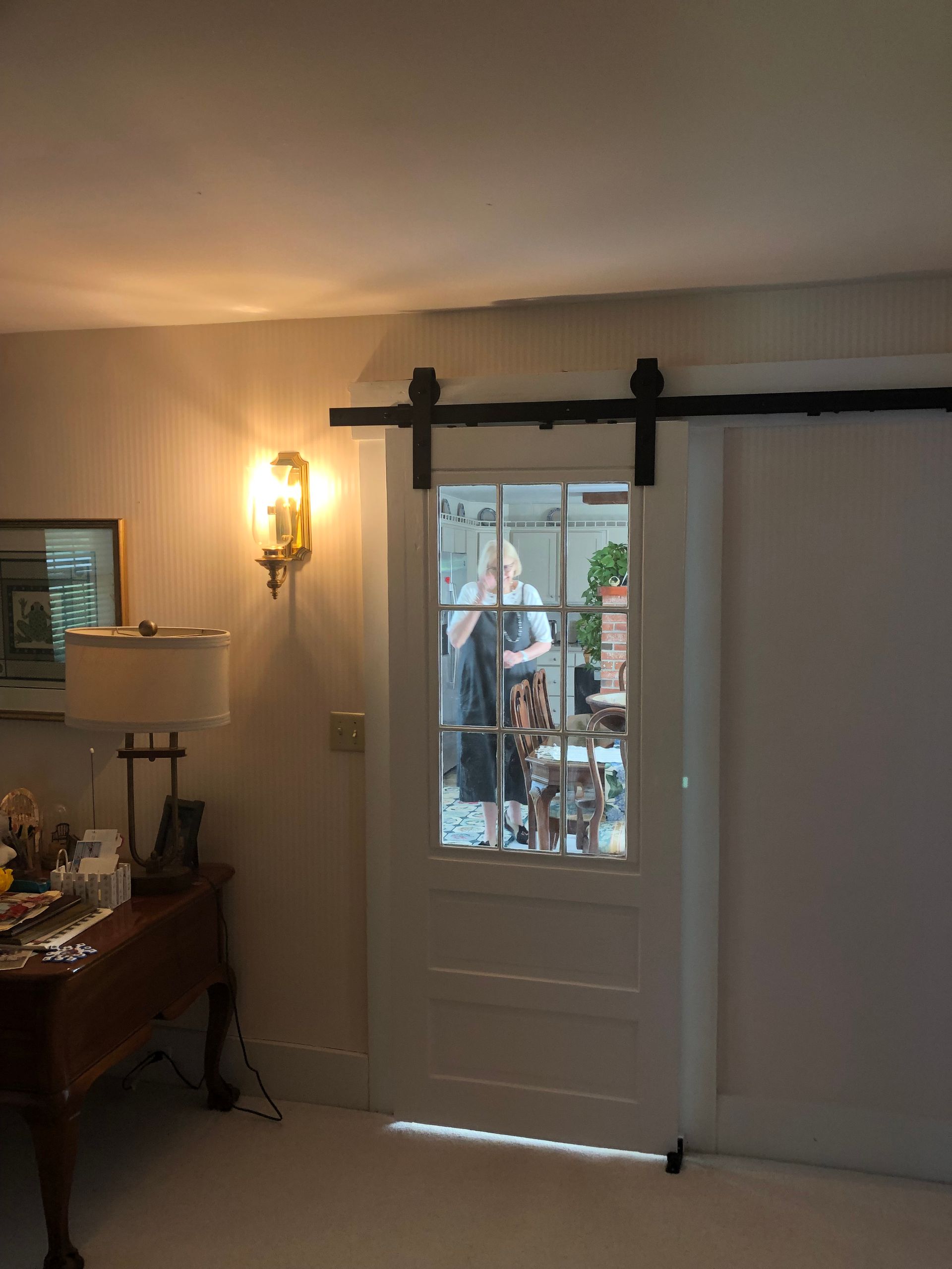 White barn door with black hardware, reflective window showing a person, mounted on a wall.
