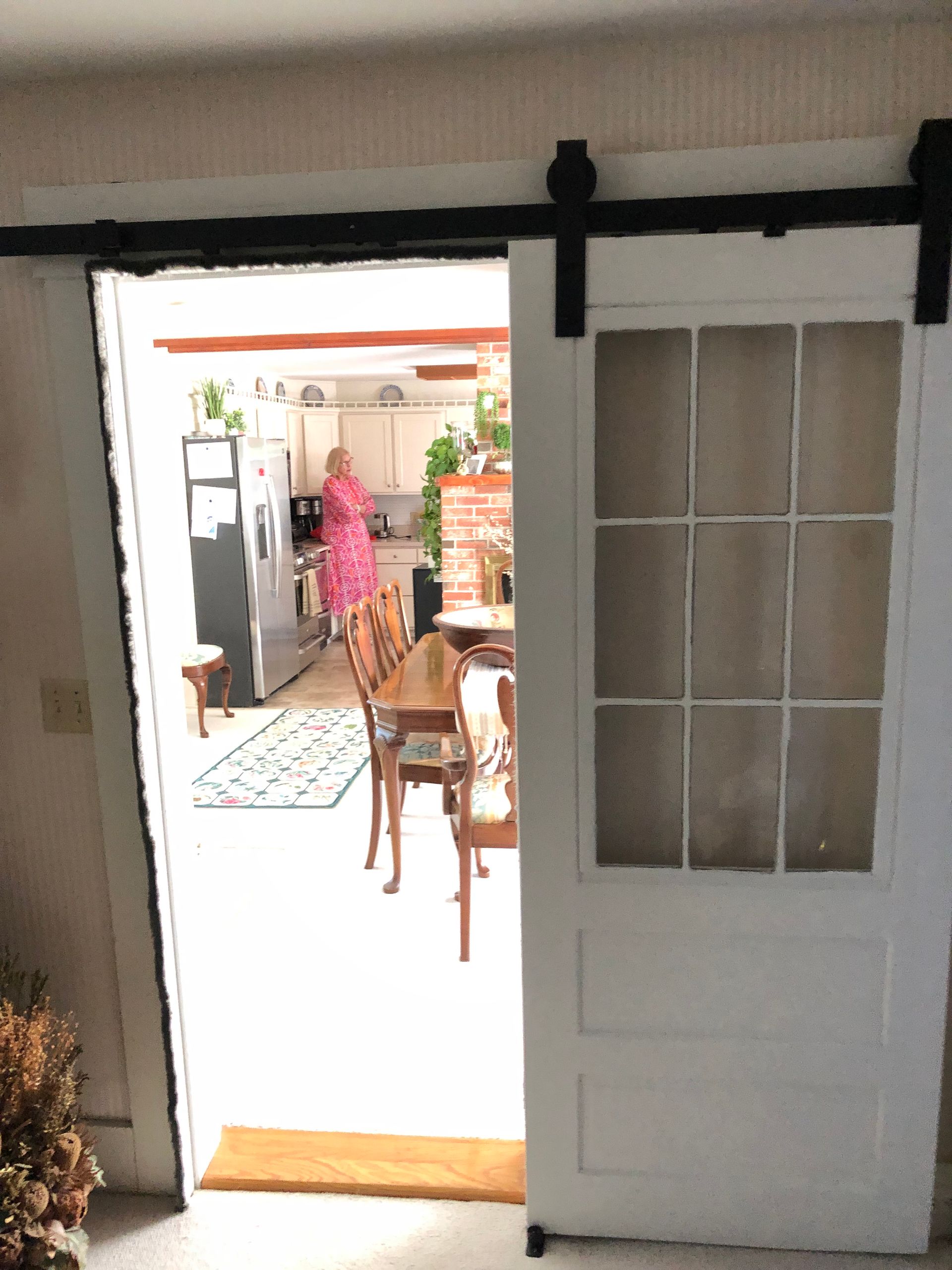 White sliding door open to a dining room and kitchen. A person in pink stands near the kitchen.