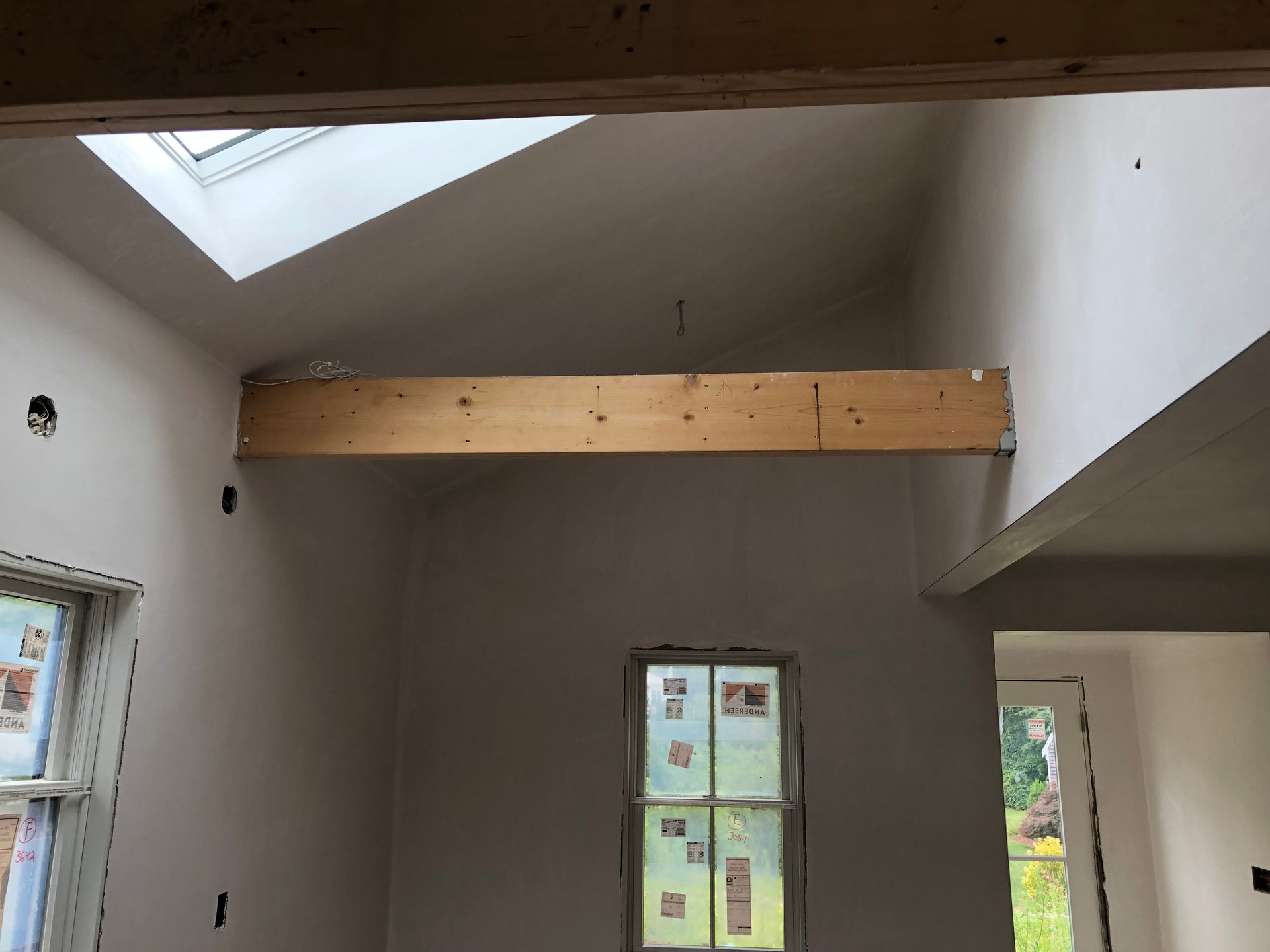 Interior view of a room under construction with a wooden beam across the ceiling and a skylight.