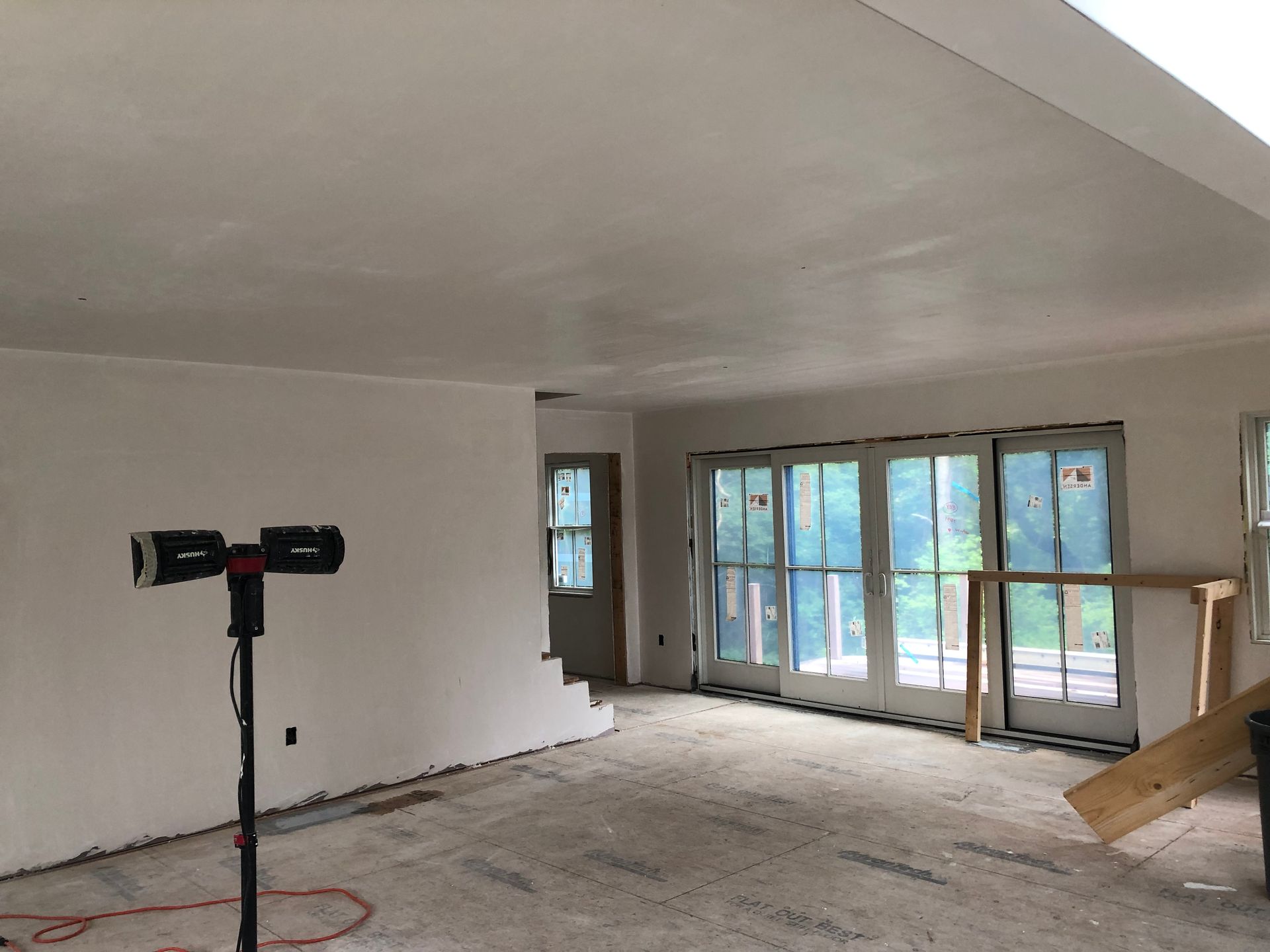 Interior of a room under construction with sliding glass doors, white walls, and a work light.