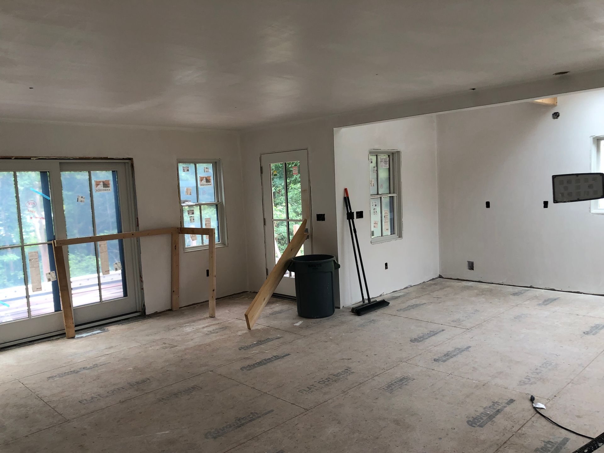 Interior of a room under construction, with white walls, windows, and doors, and protective flooring.