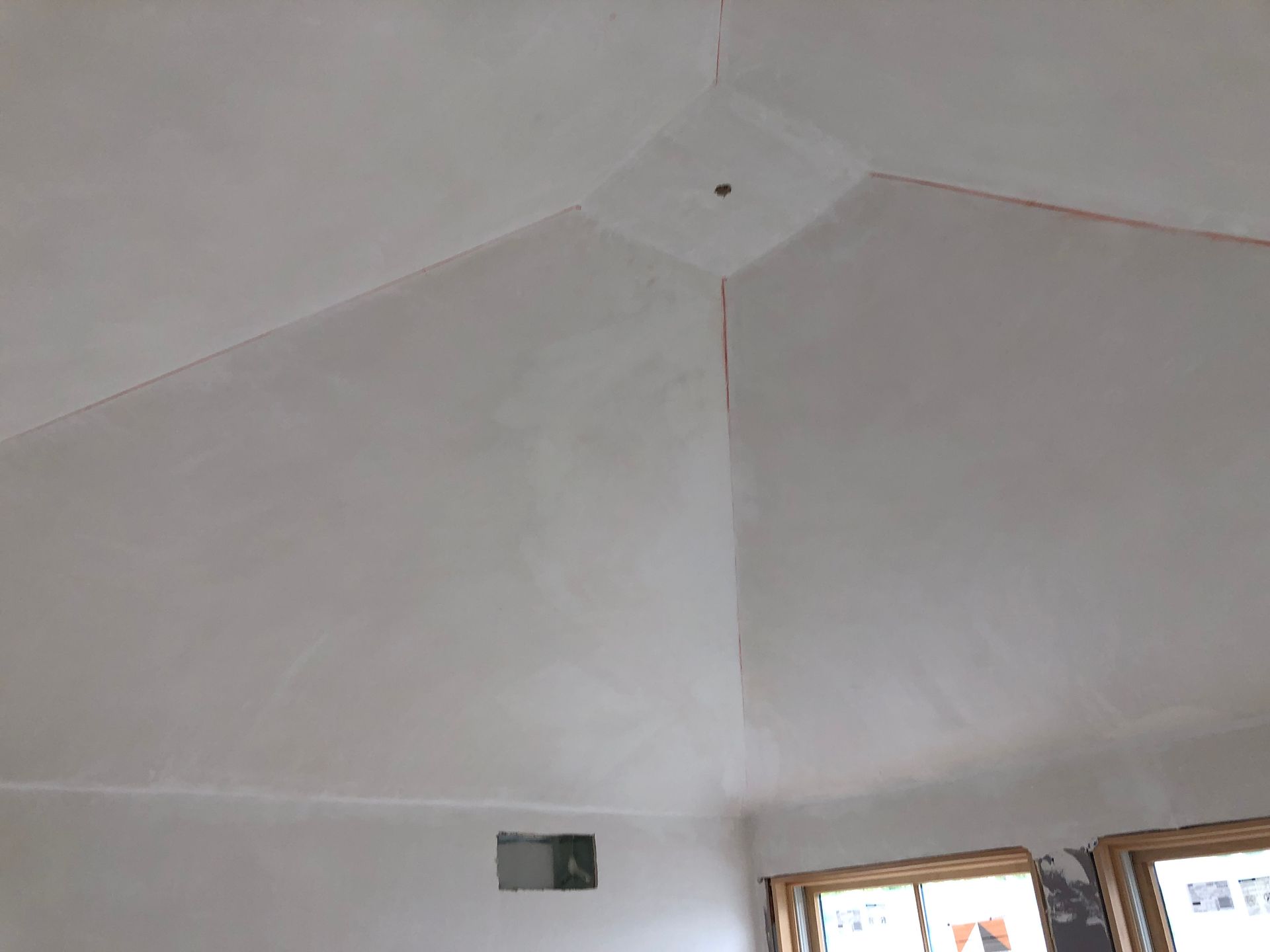 White, angled ceiling with a light fixture, visible in a room with a window frame.