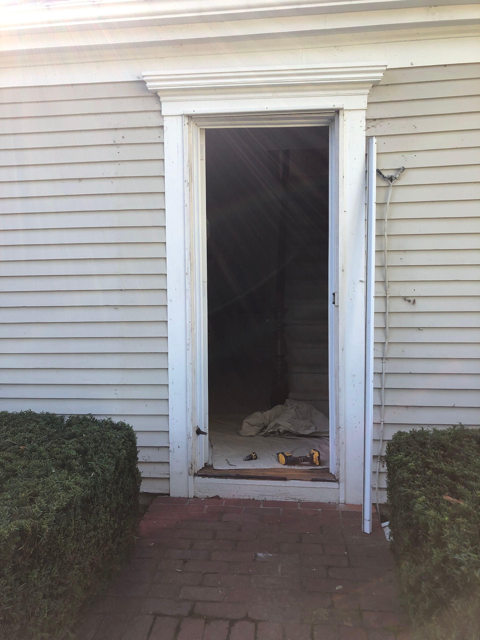 An open doorway in a gray clapboard building. Exterior shot, the door frame is white, dark interior.