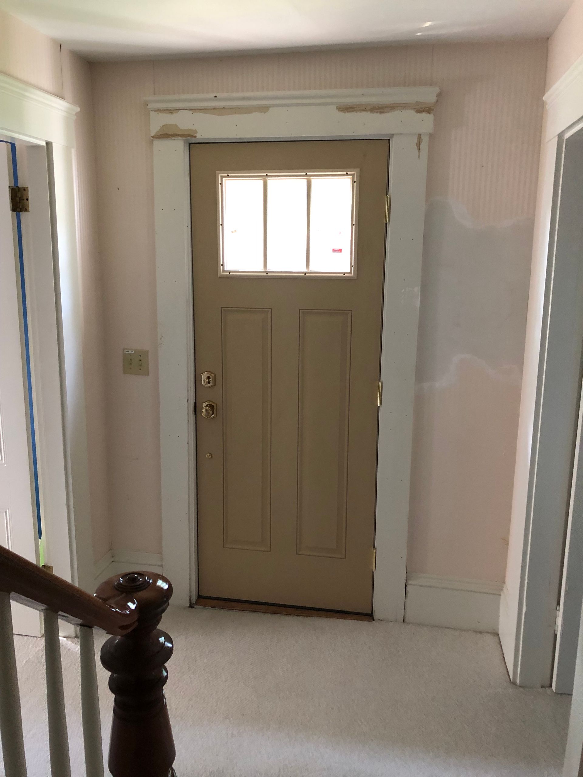 Beige door with glass window and white trim in a hallway with pink walls and carpet.