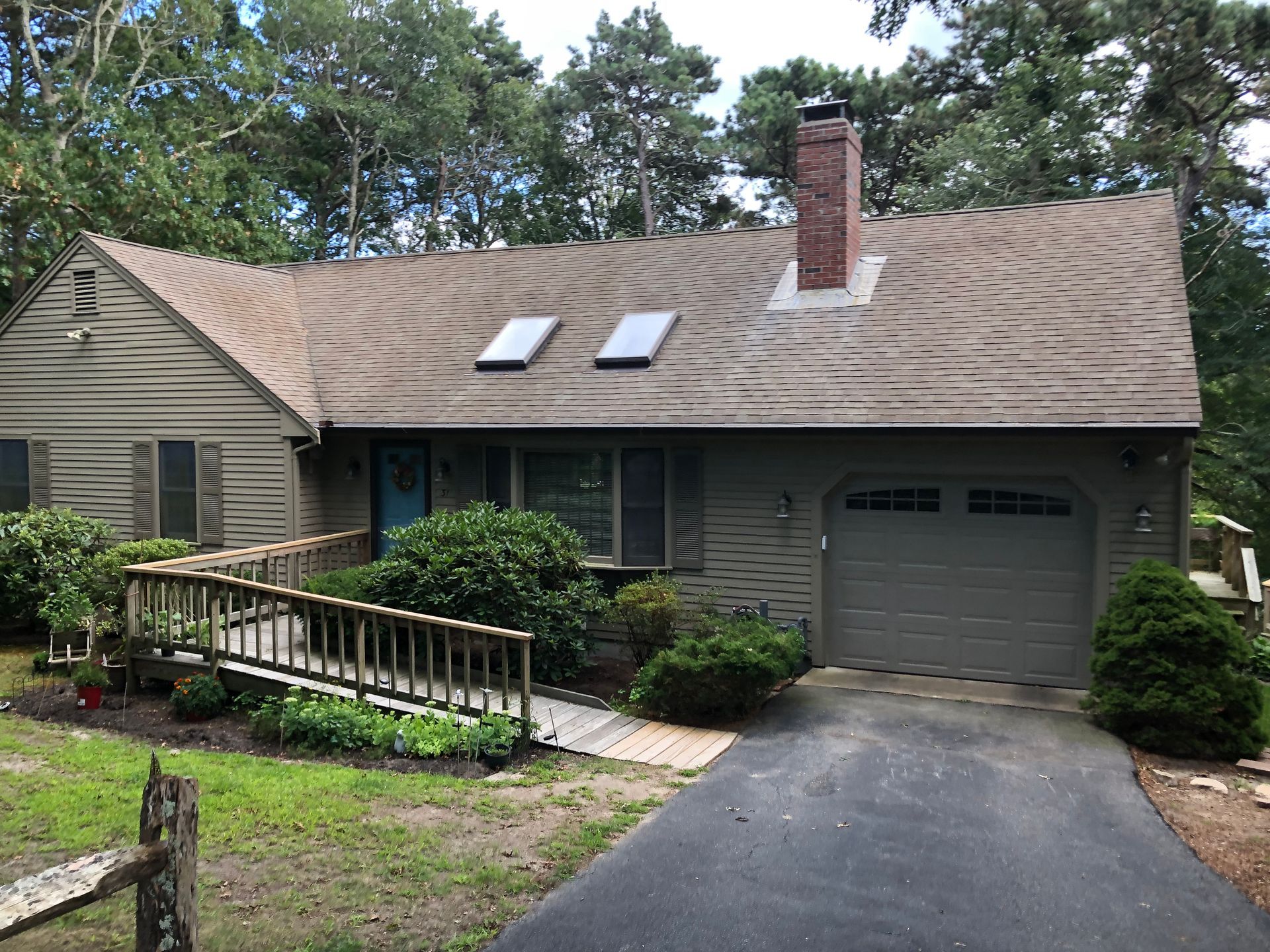 Tan-colored house with a ramp leading to the front door. Garage and brick chimney are visible. Overcast day.