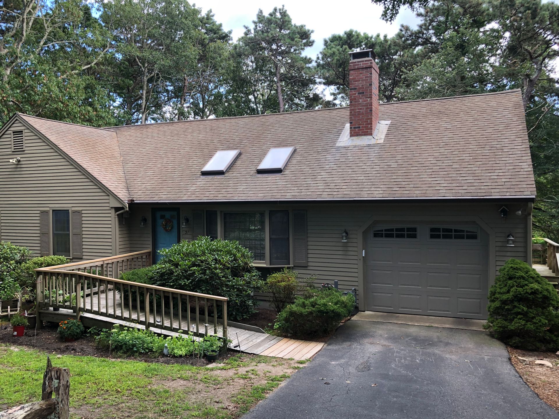 Green house with a ramp and a gray garage door, brown roof.