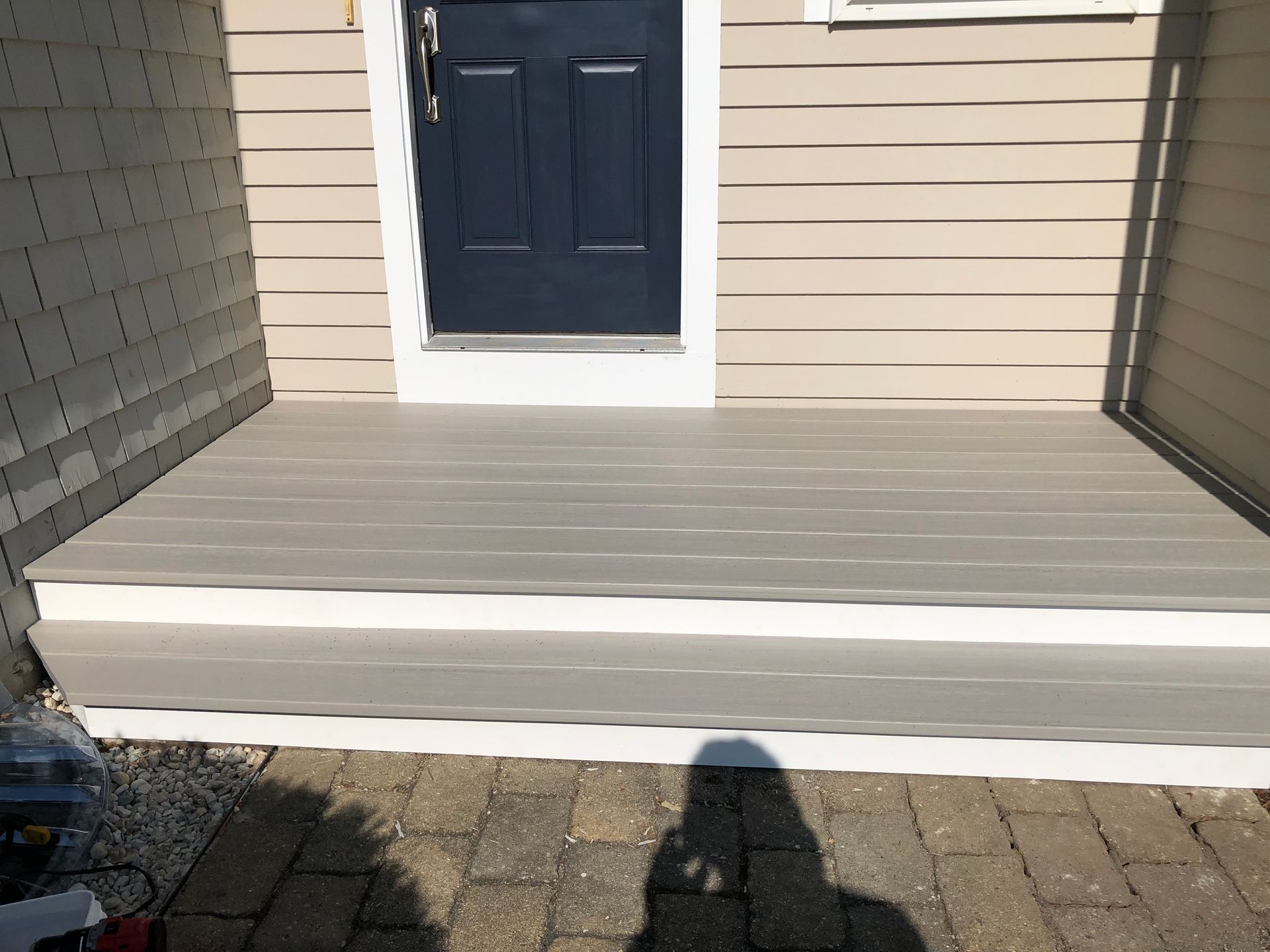 A small, gray wooden porch with white trim and a dark blue door.