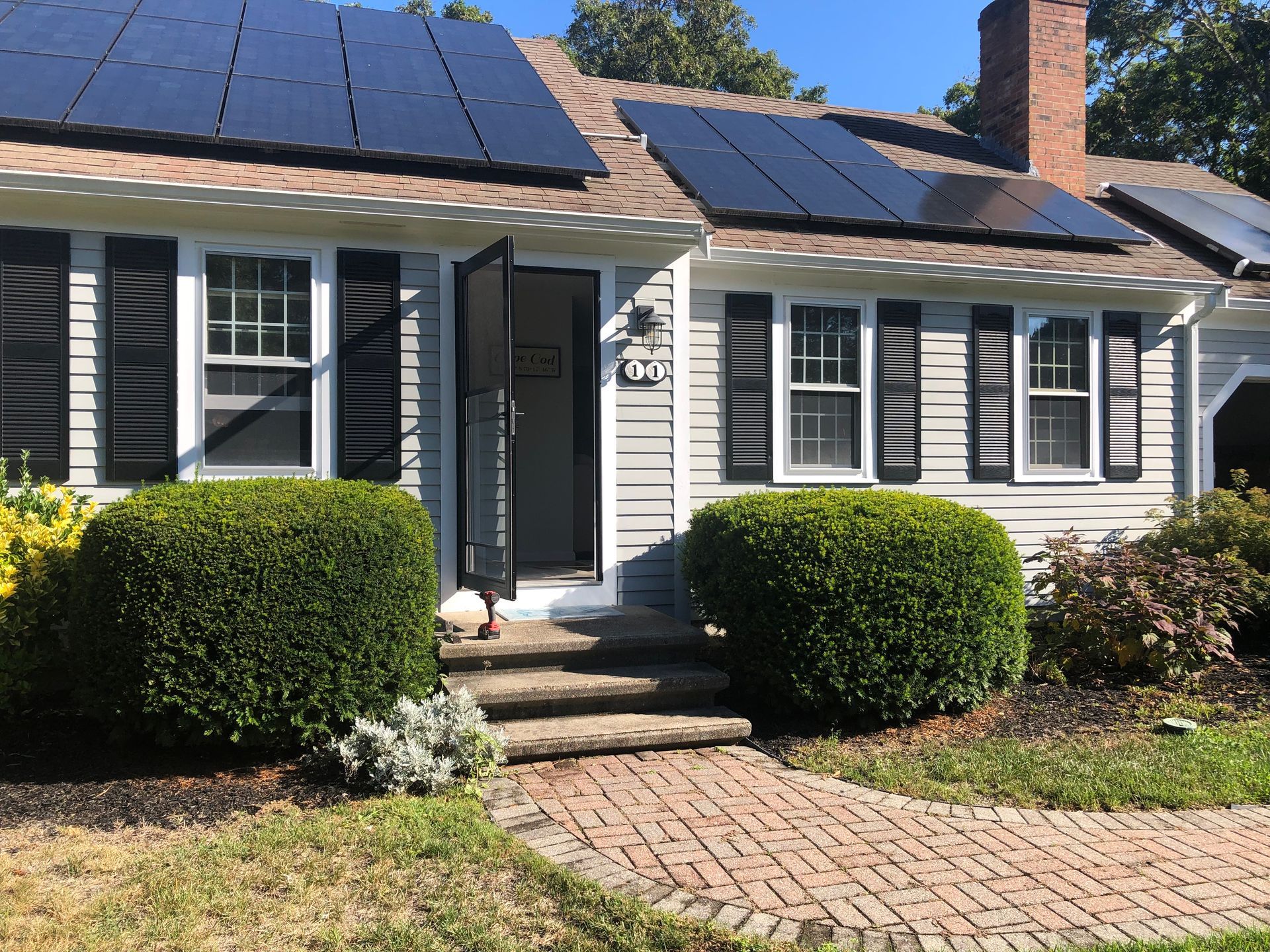A house with solar panels on the roof, black shutters, and a brick pathway.