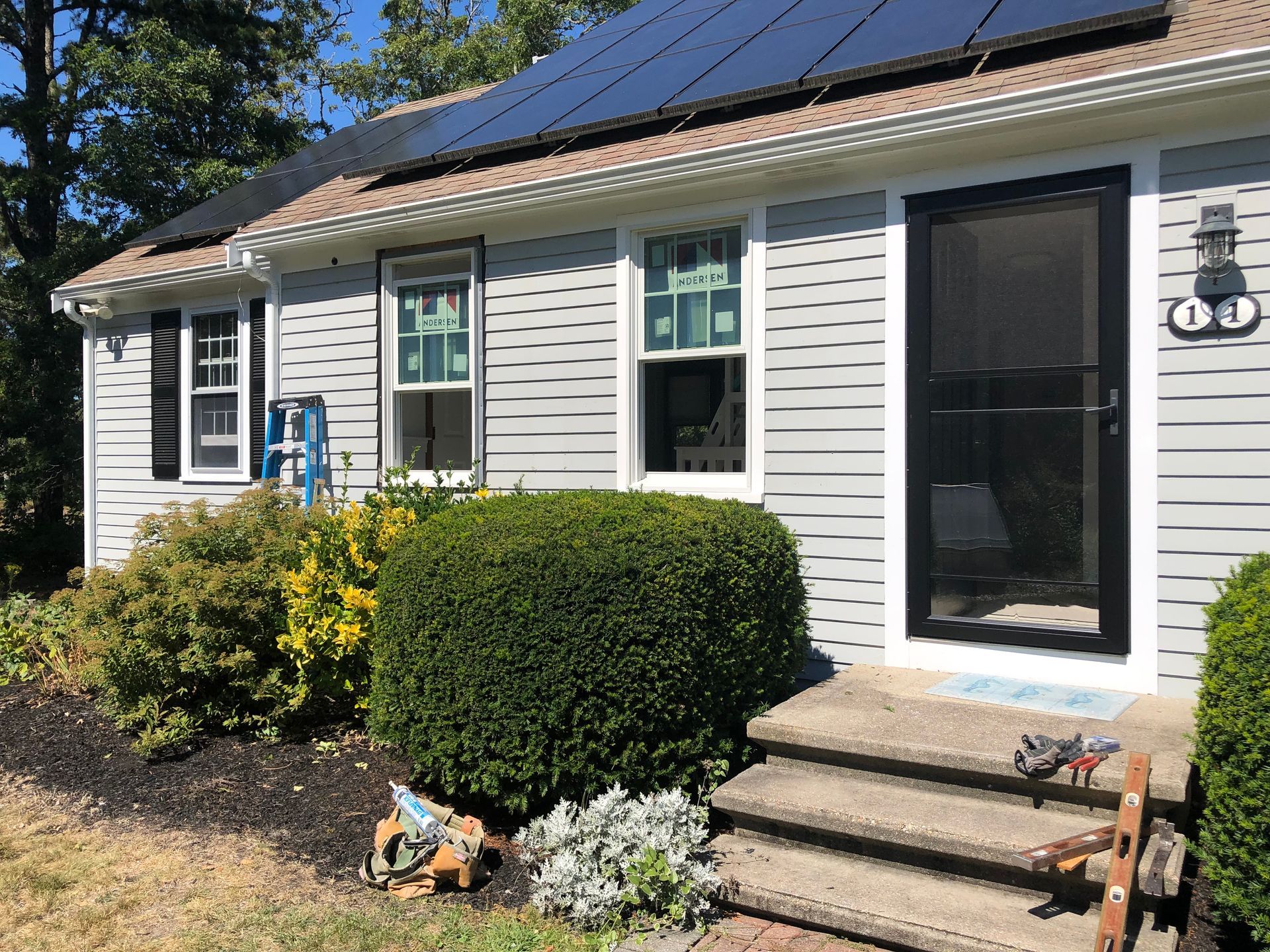 House with solar panels on roof, gray siding, new windows, and black front door. Landscaping in front.