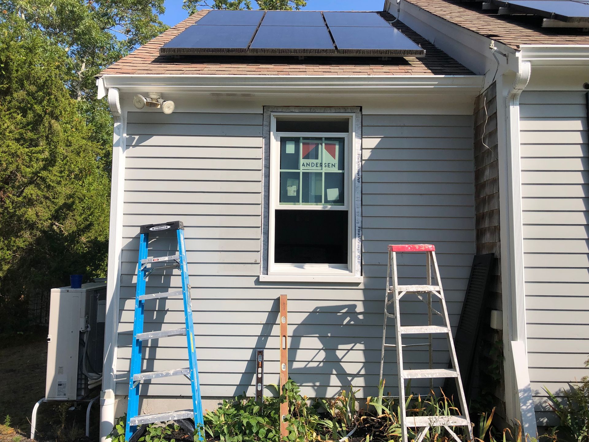 A building with solar panels, a new window being installed, and two ladders.
