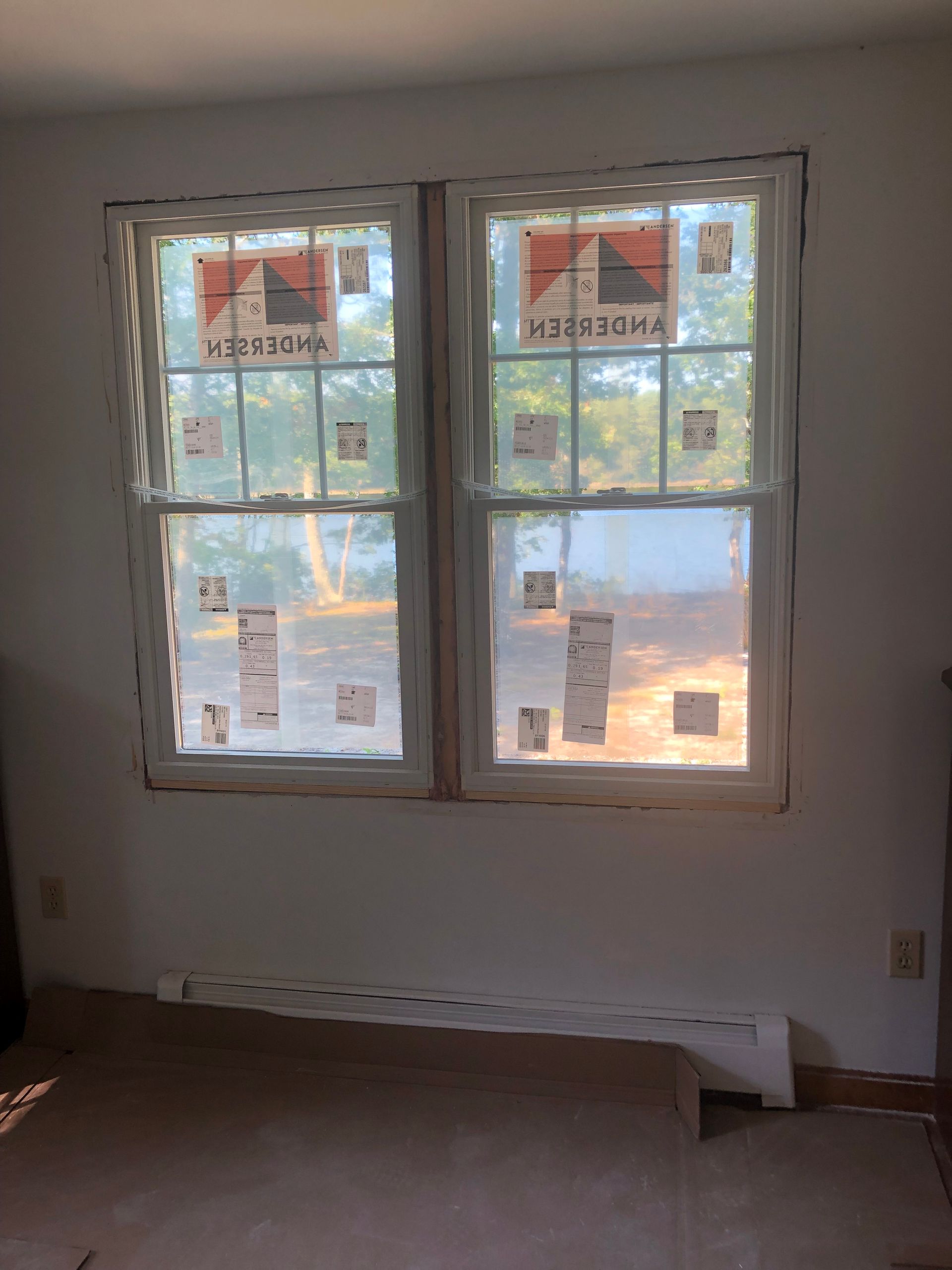 Two white double-hung windows in a room with protective paper, white walls, and a radiator underneath.
