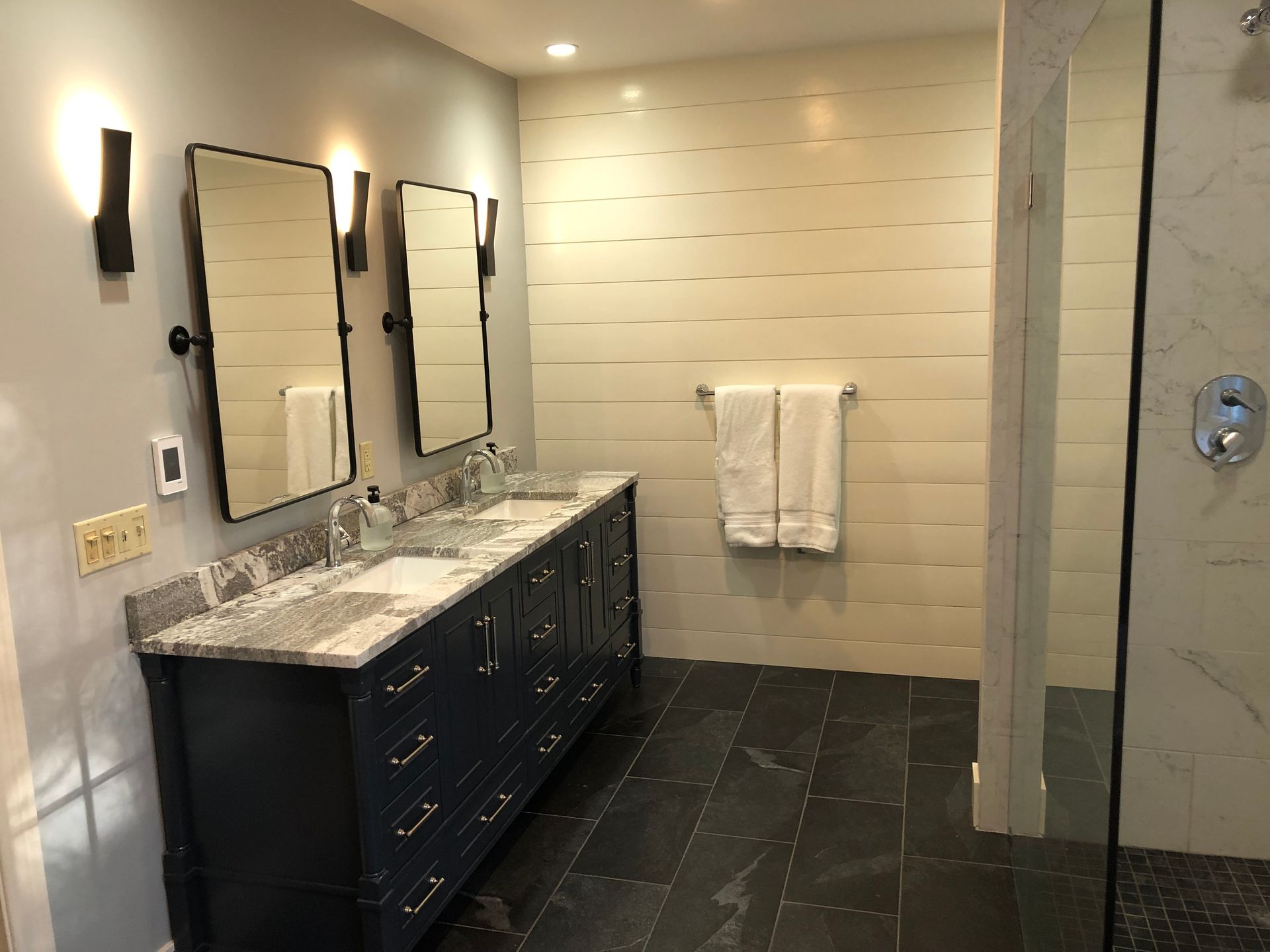 Bathroom with navy vanity, two mirrors, white tile wall, and glass shower.