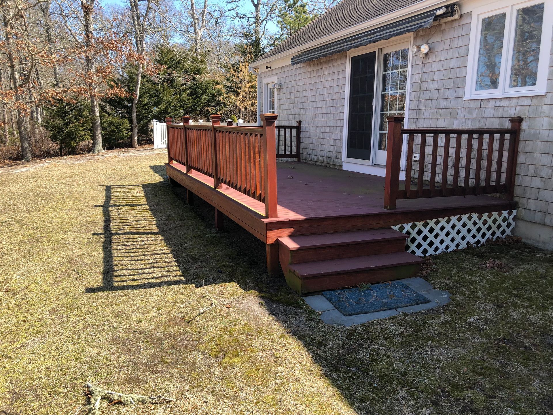 Wooden deck attached to a house with steps. Reddish-brown railings and deck, white lattice underneath.