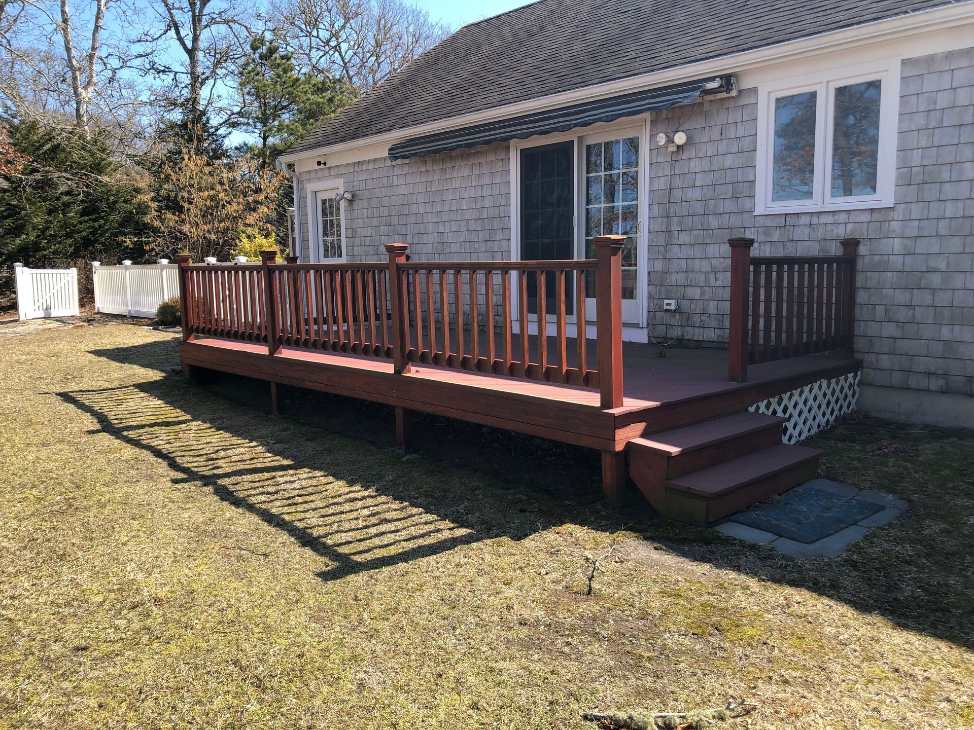 Wooden deck with red stain, attached to a gray-sided house with a sliding door and windows.