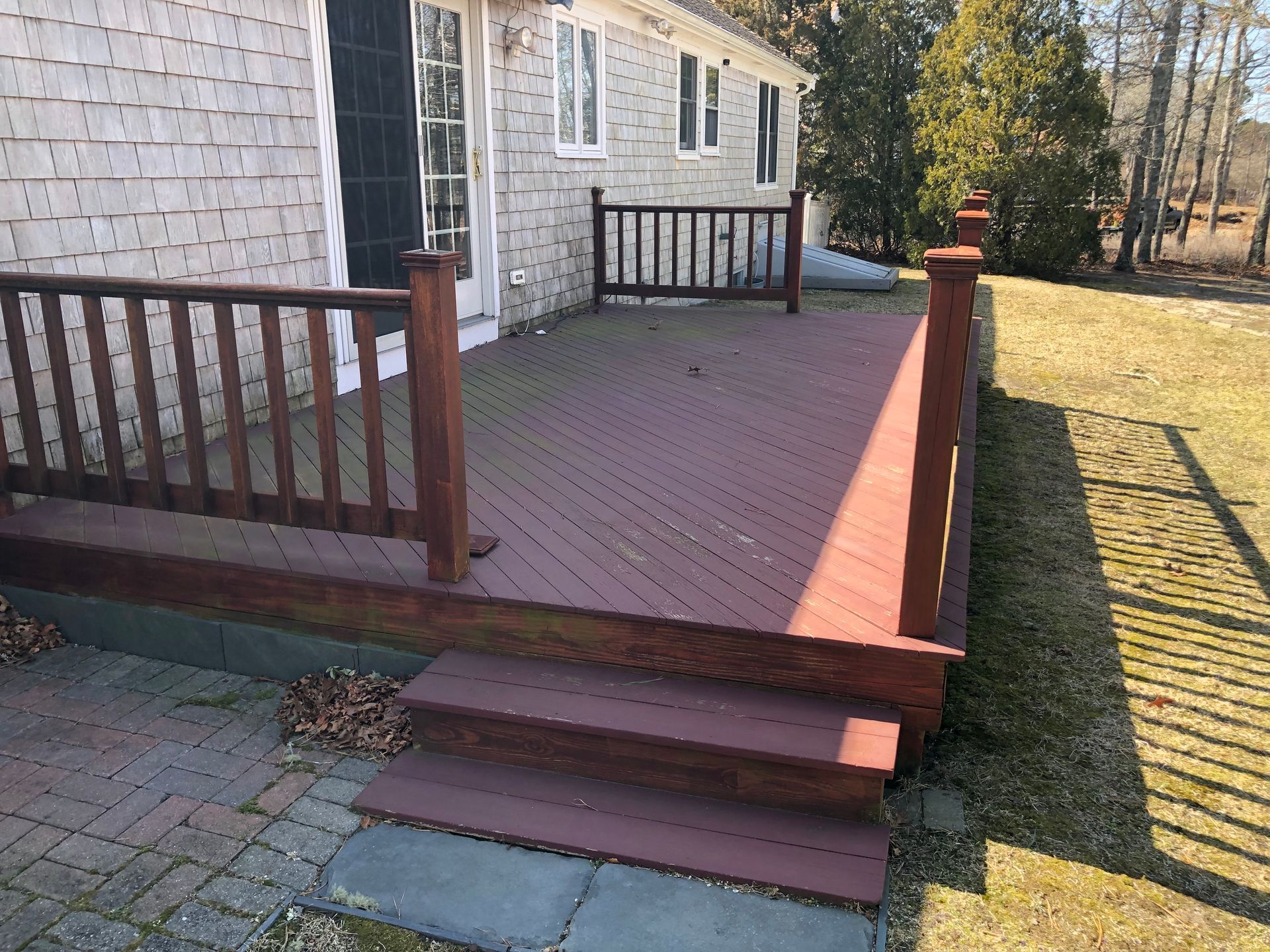 Red wooden deck with steps attached to a light-colored house.