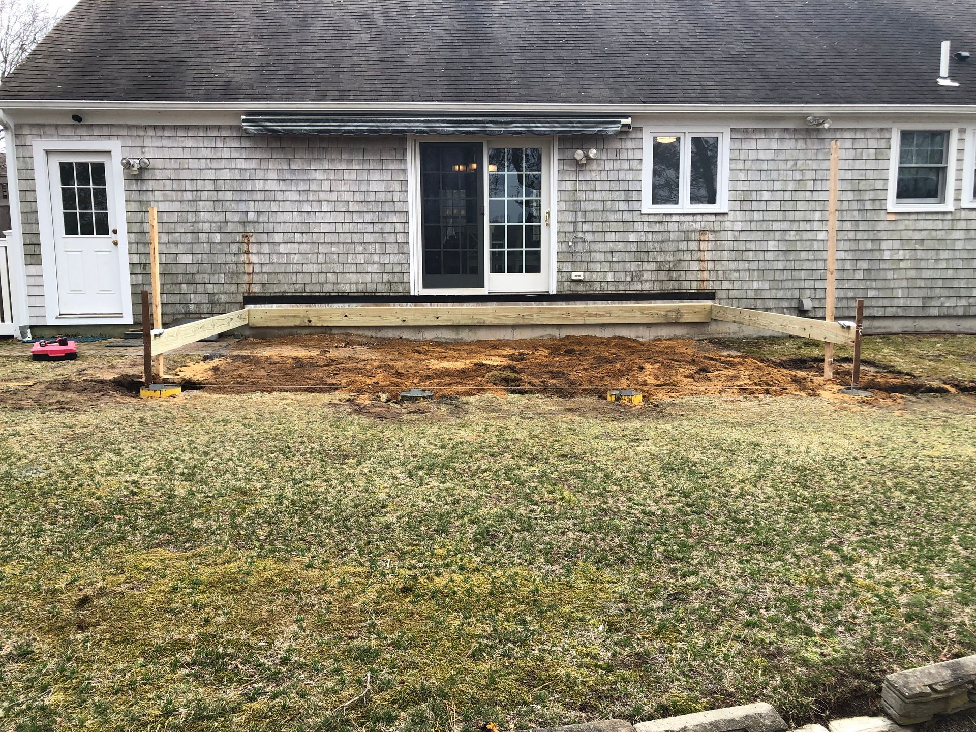 Backyard, partially built wooden deck with a sliding glass door and clapboard siding.