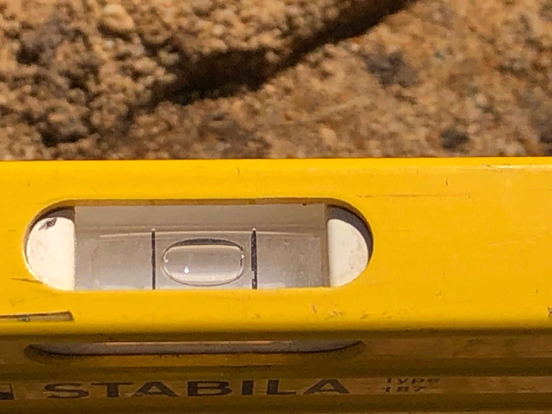 Yellow level with bubble centered, resting on a textured brown surface.