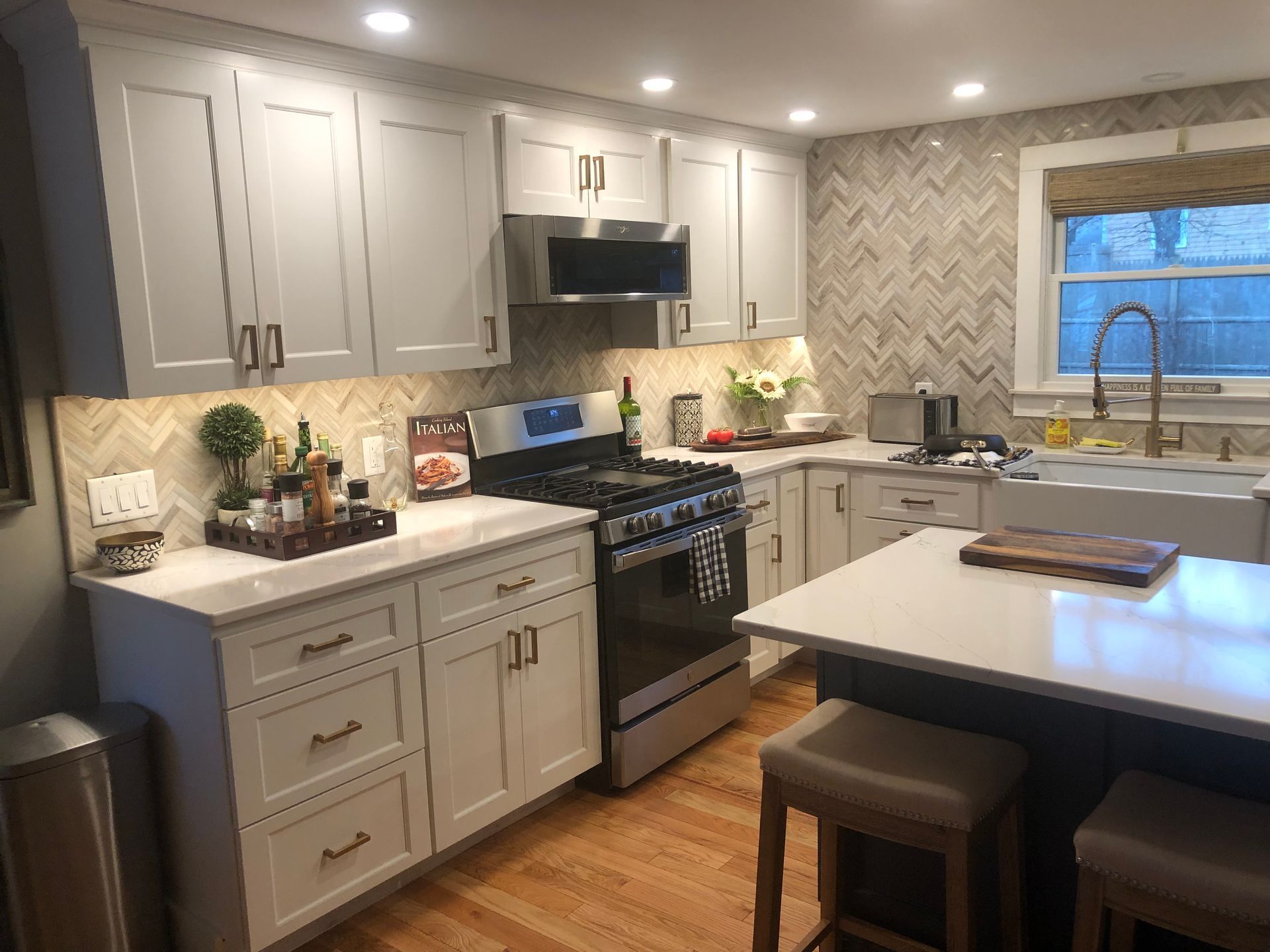 Bright white kitchen with white cabinets, stainless steel appliances, and herringbone backsplash.