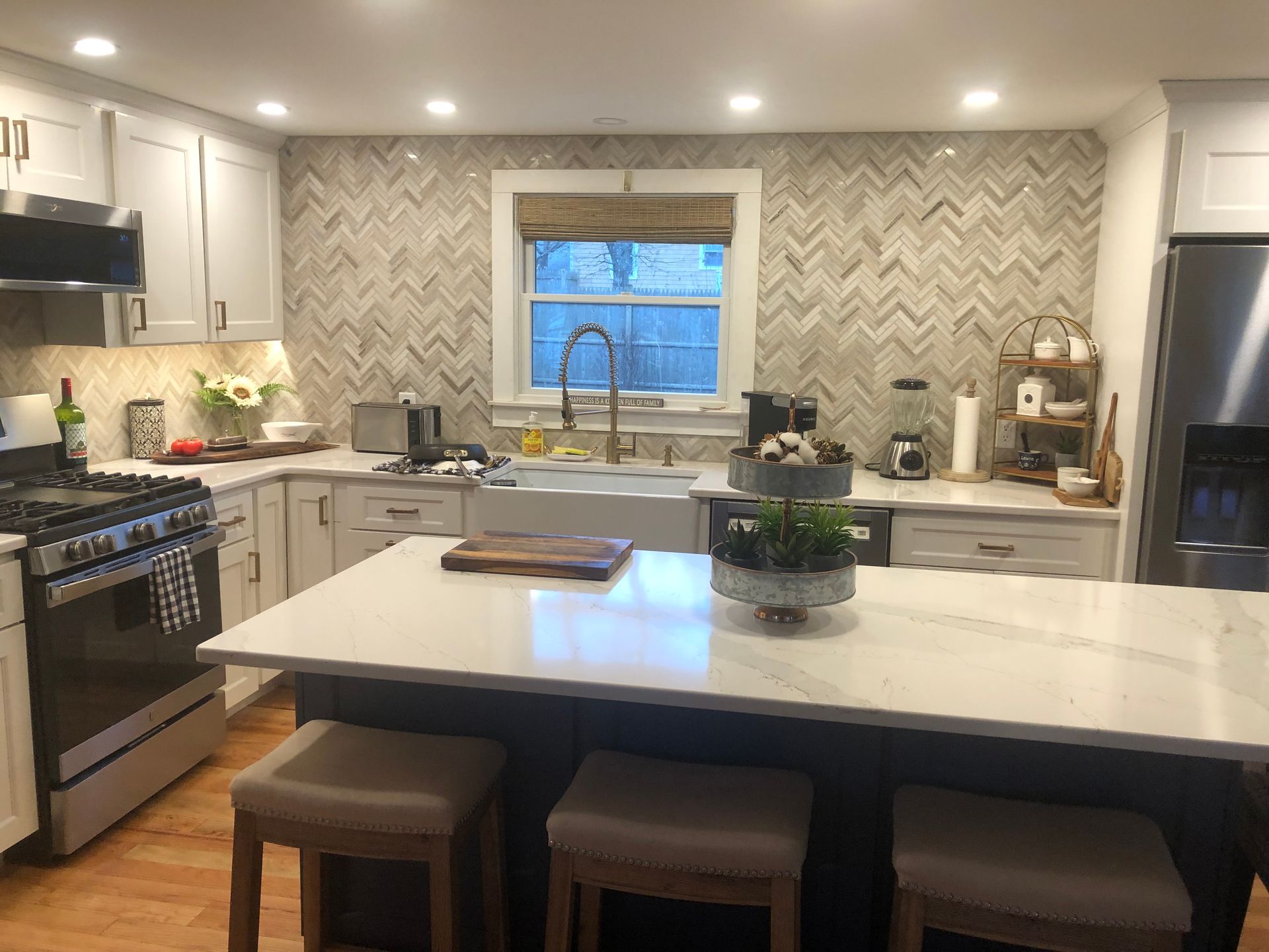 Kitchen with white cabinets, marble countertop island, herringbone backsplash, and a farmhouse sink.