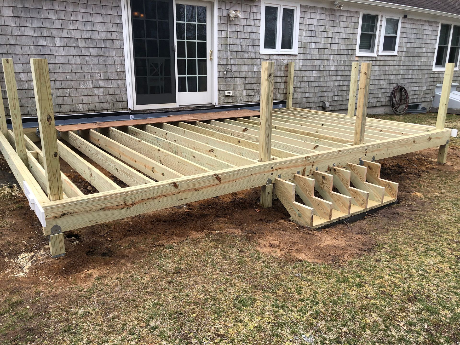 Partially built wooden deck with steps, attached to a house with shingle siding.