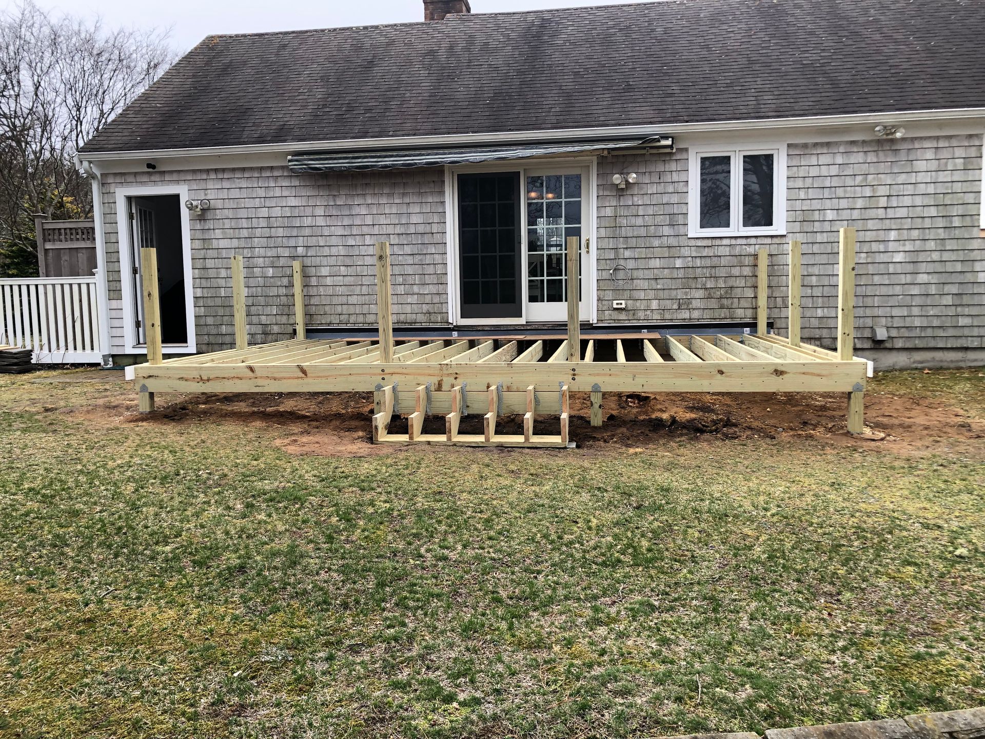 Newly built wooden deck with steps attached to a shingle-sided house; lawn in the foreground.