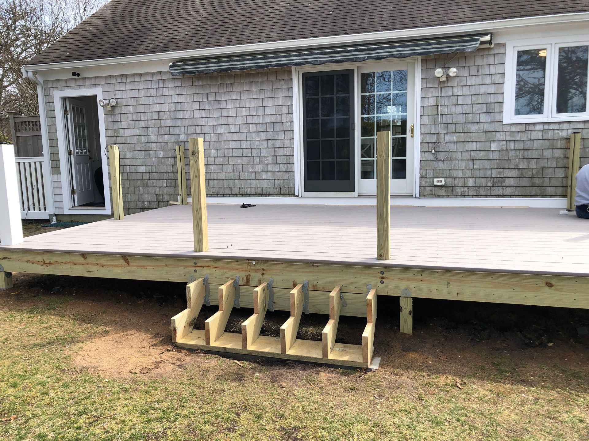 Wooden deck under construction with unfinished steps, attached to a house with a sliding door.