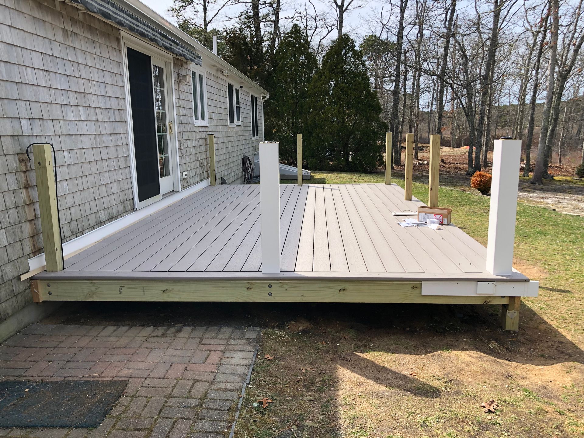 A partially built deck with gray composite decking, white posts, and lumber framing, next to a house.