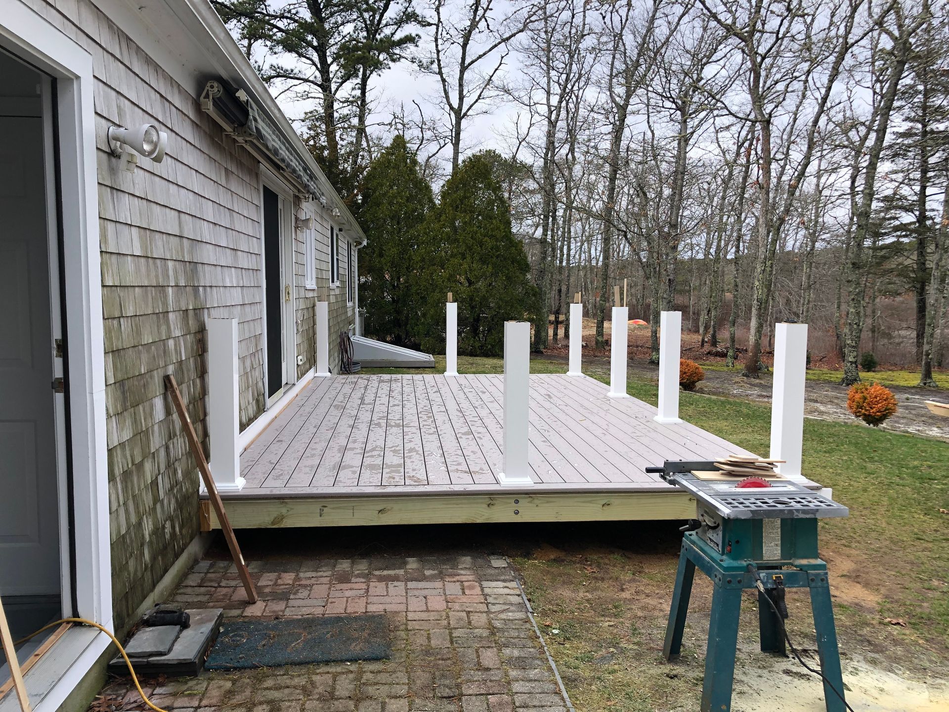 Deck under construction with white posts, gray deck boards, and a green saw.