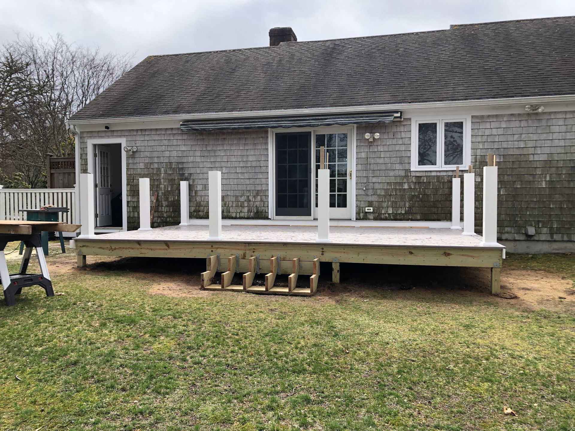 Backyard deck with white railing, built onto a house with white siding, on a grassy lawn.