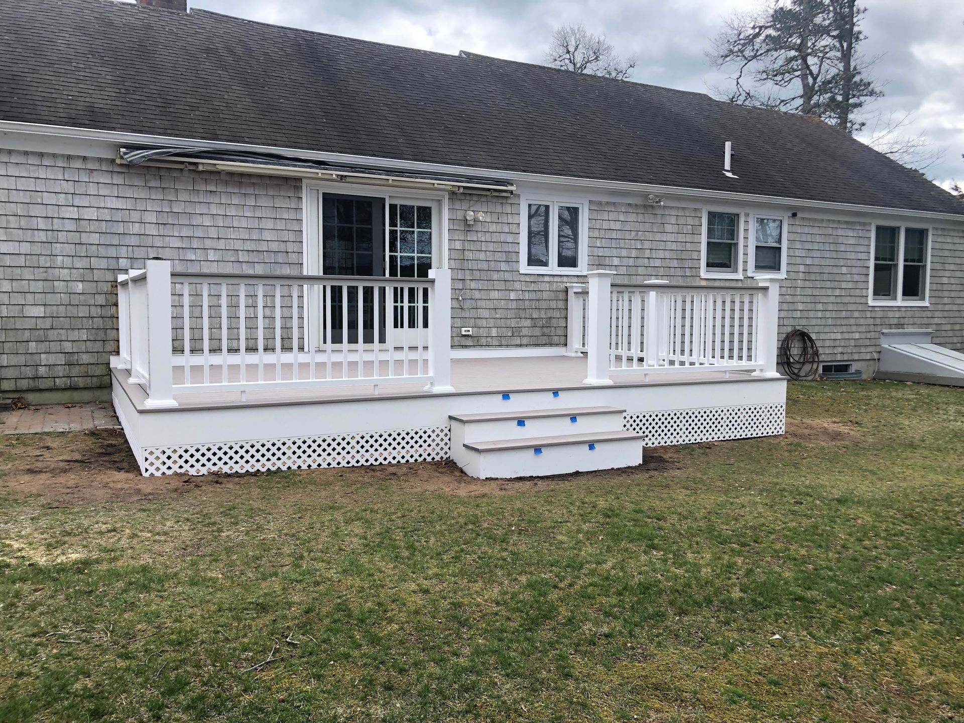 Backyard deck with white railing and steps leading to a grass yard, attached to a gray house.
