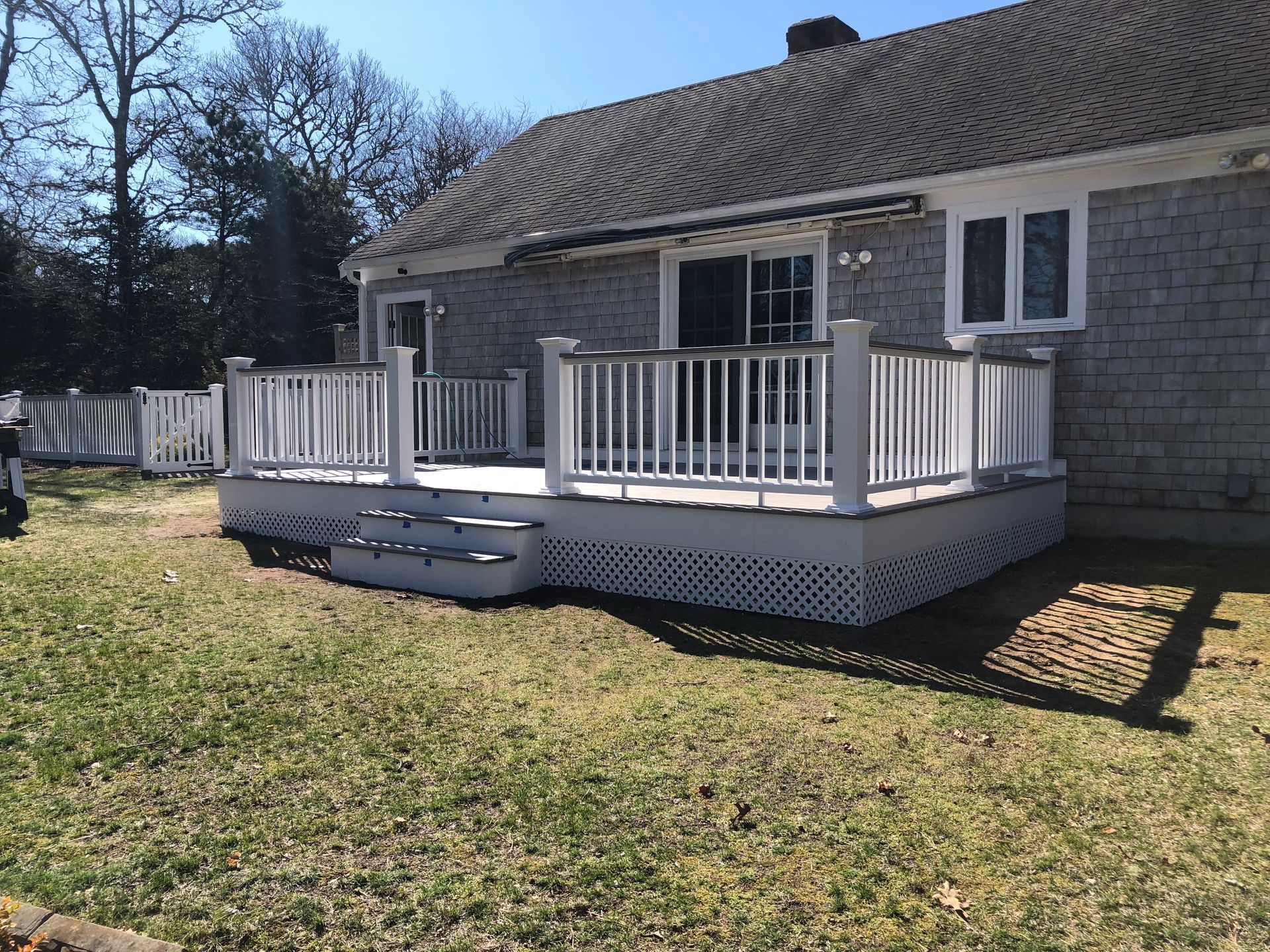 White wooden deck with railings, steps, attached to a gray-shingled house, surrounded by grass.