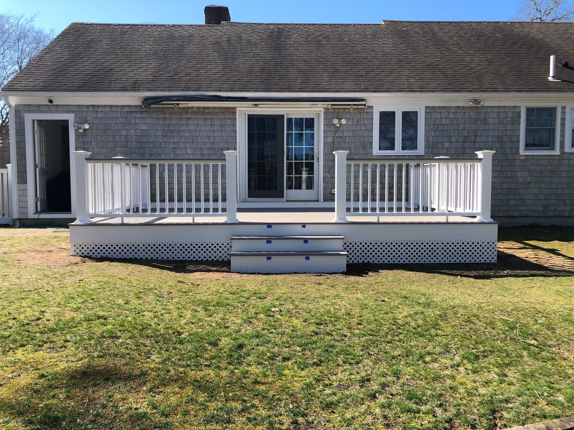 White deck with railing, stairs, and sliding glass door on a house with a shingle roof.