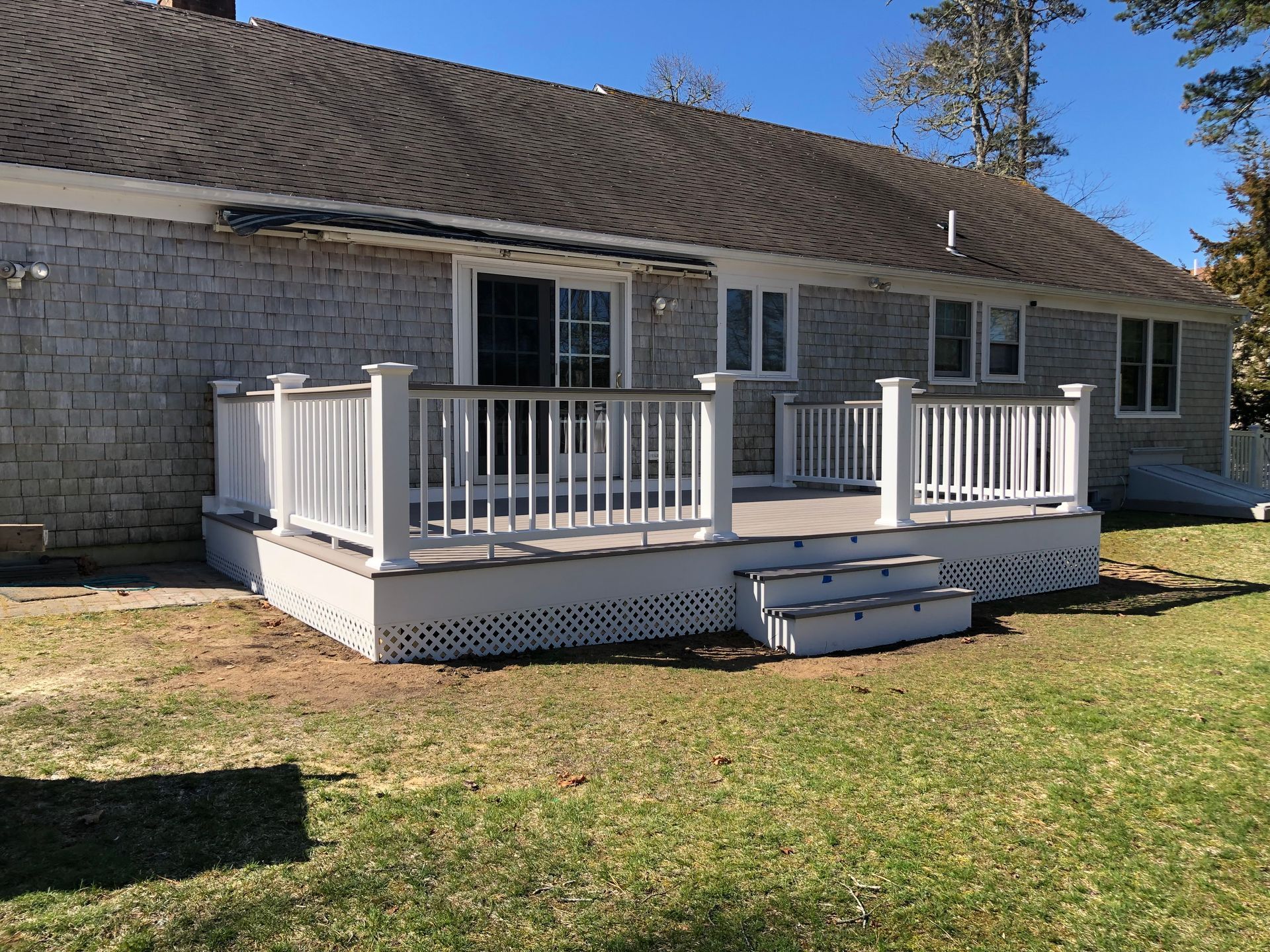 Back of a house with a white deck and steps, gray shingle siding, and a grassy yard.
