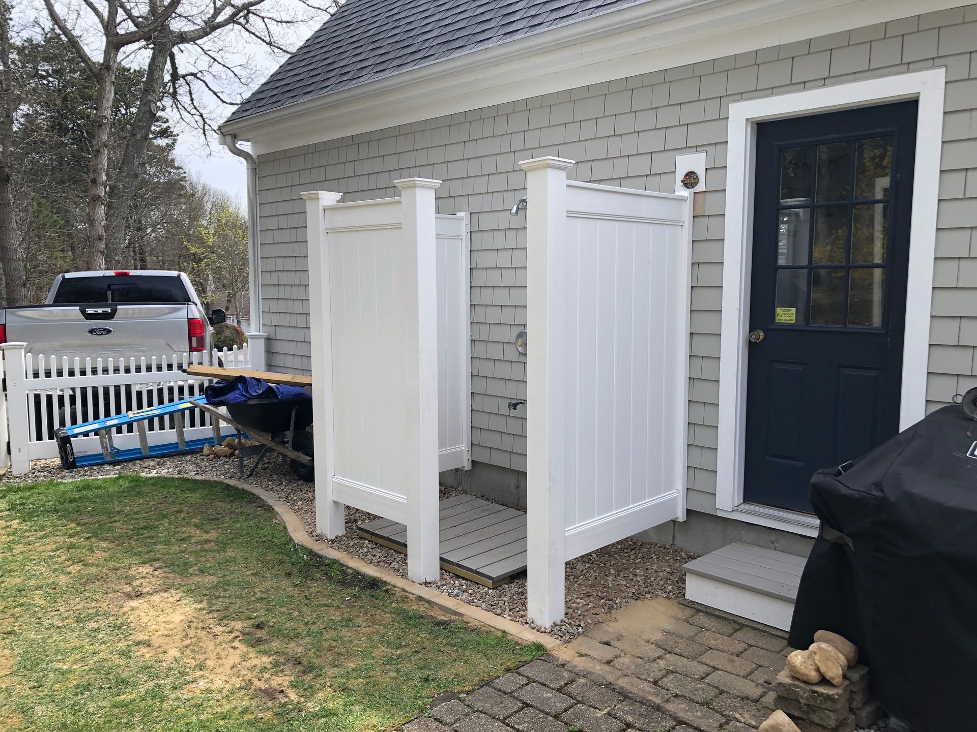 Outdoor white shower enclosure next to a blue door. A truck is in the background.