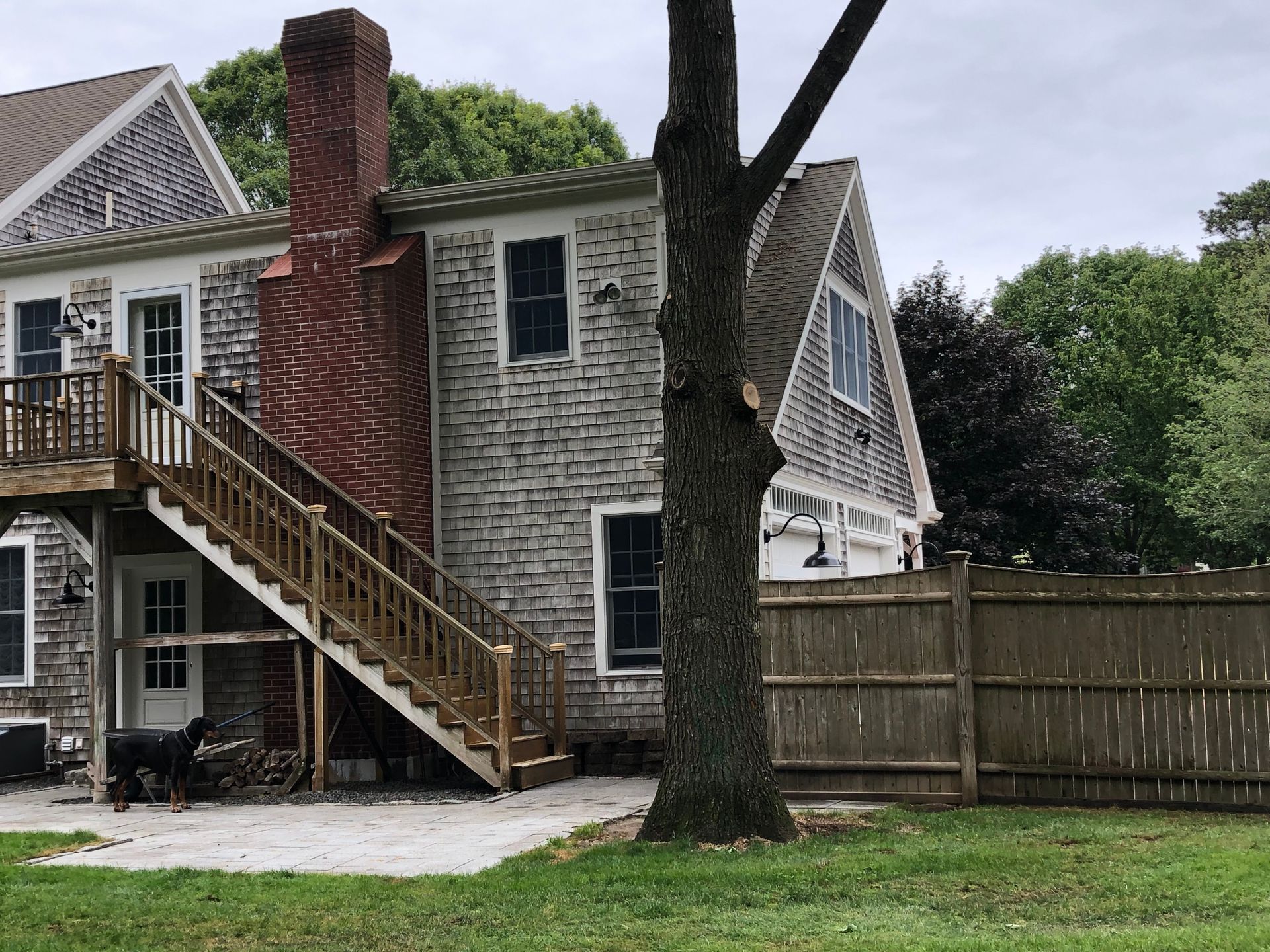 House exterior with gray shingles, wooden staircase, red brick chimney, and a wooden fence.