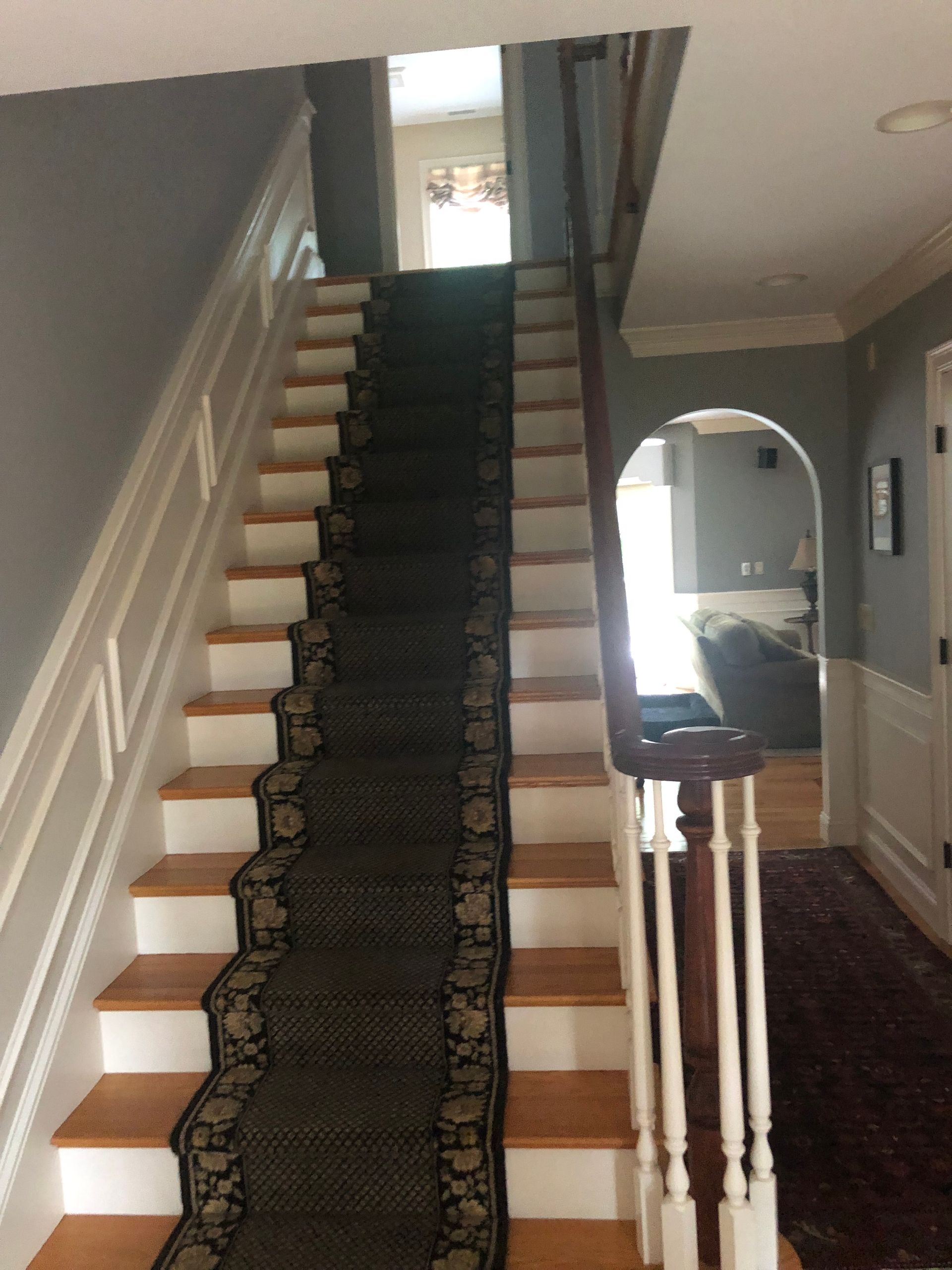 Staircase with wooden steps, carpet runner, and white banisters. Gray walls and doorway in view.