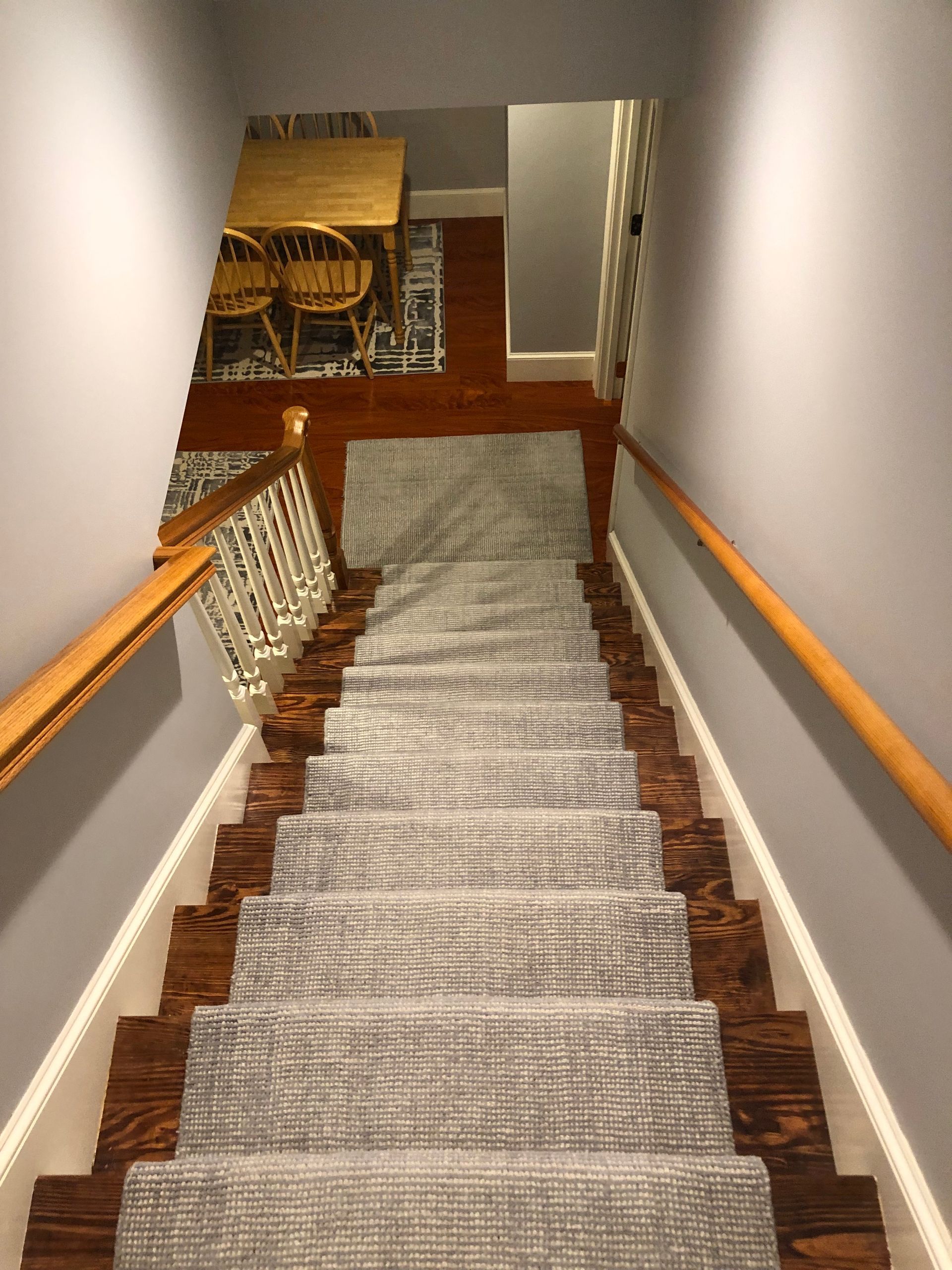Staircase with gray carpet runner and wood stairs, leading down to a room with a table and chairs.
