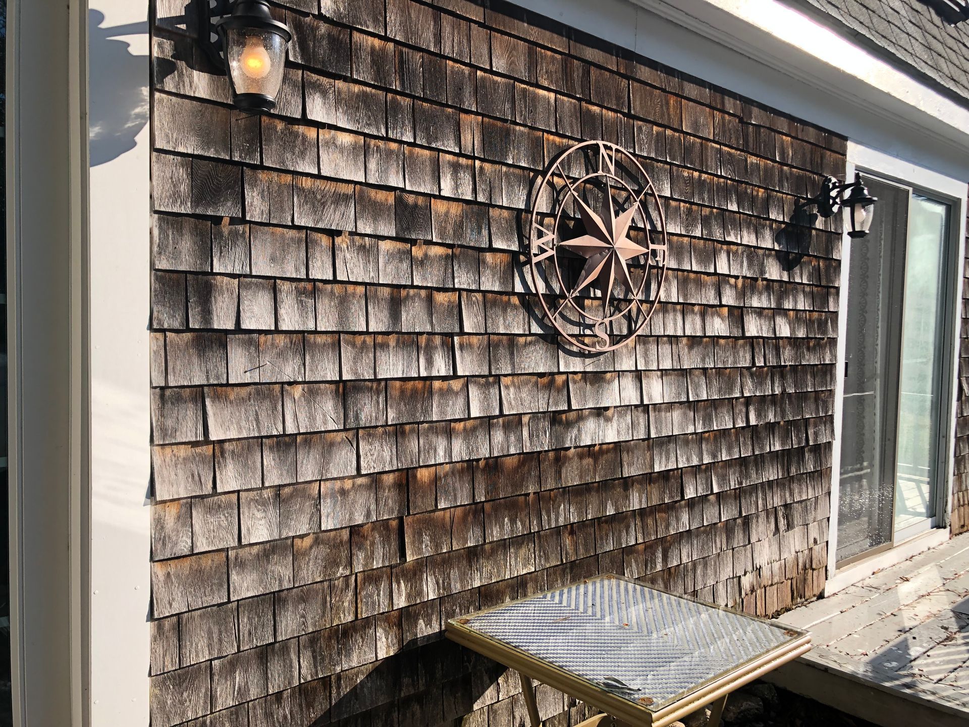 Wooden shingle siding with a starburst decoration and two sconces; a table sits below.