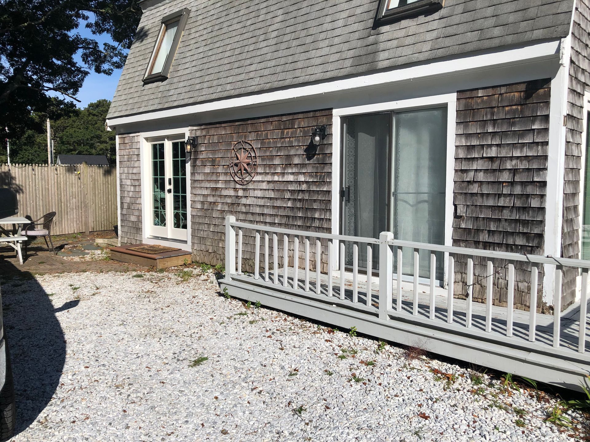Exterior of a weathered gray-shingled building with a small deck and gravel yard.