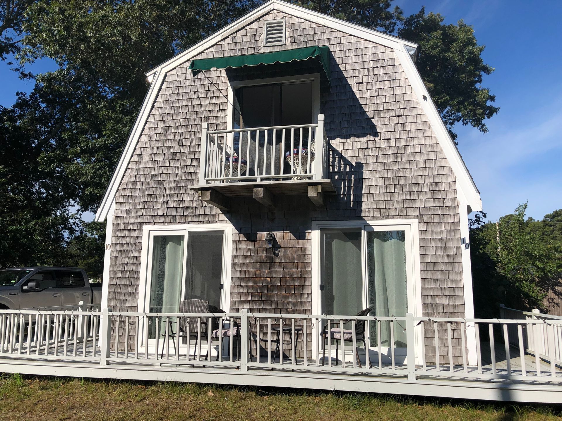 Gray shingled building with a balcony and two sliding glass doors, white railing, green awning, sunny outdoor setting.