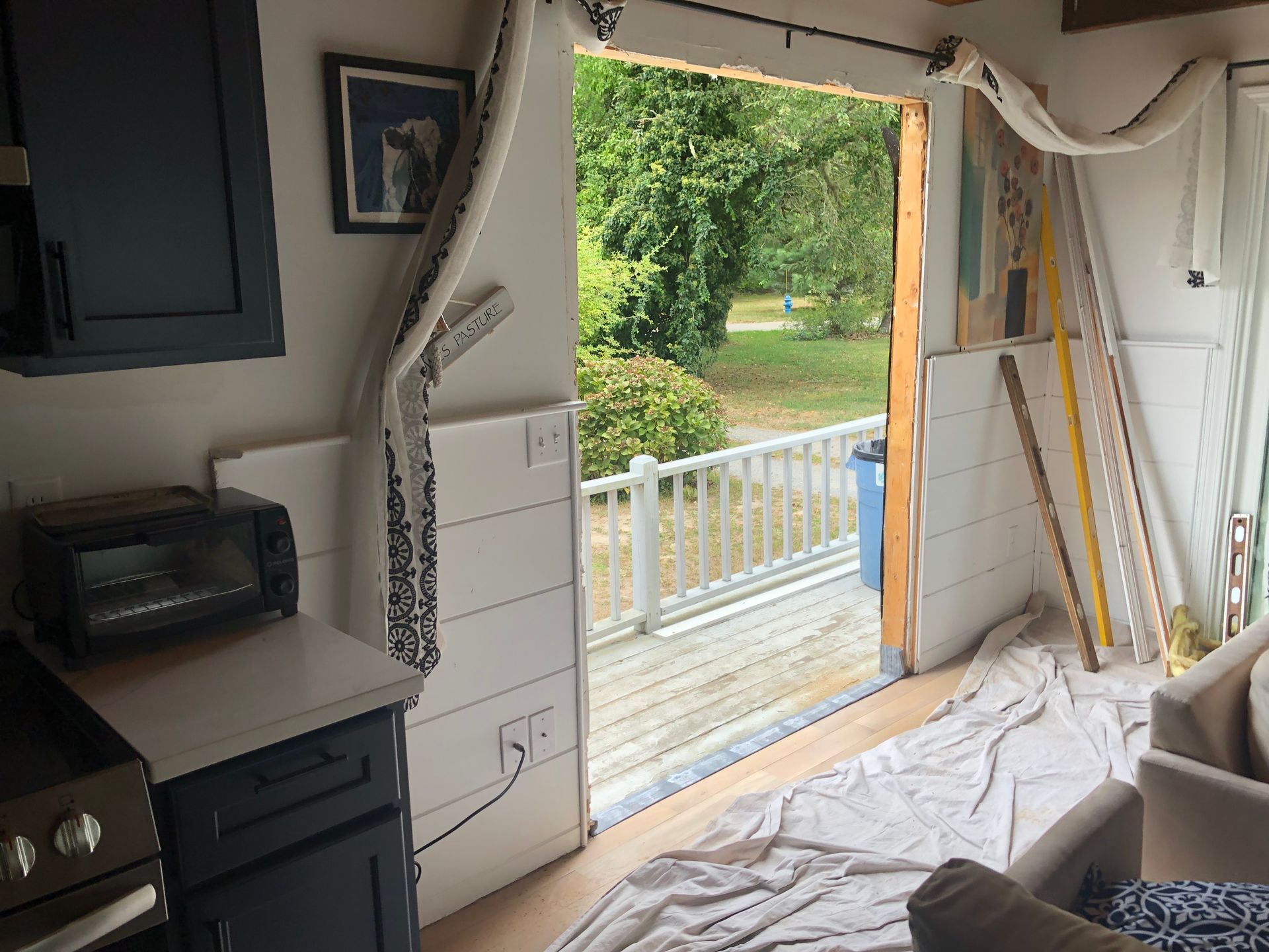 Interior view of a small kitchen with a partially open door to a porch. White paneling and blue cabinets are visible.