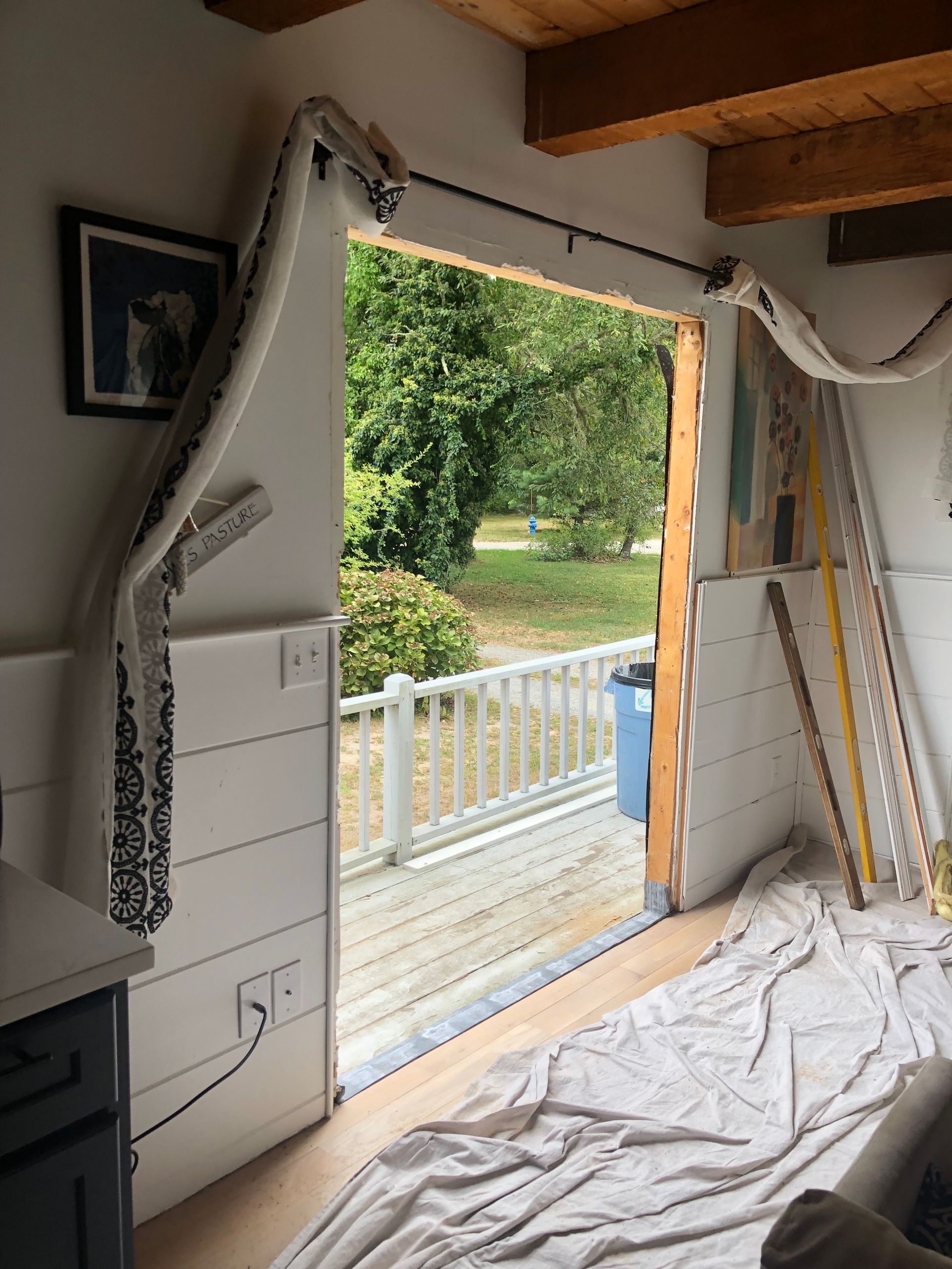 Interior doorway open to a deck and yard. Curtains hang from a rod. Construction in progress.