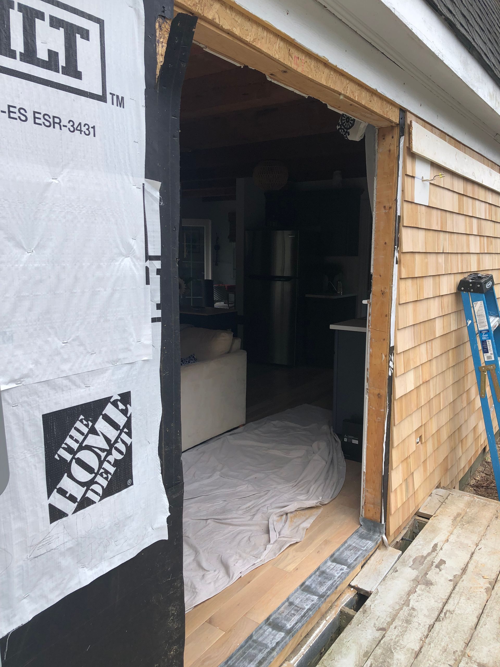 Exterior view of a doorway, unfinished, with siding and interior visible. Black wrap, white, wood, and a deck.