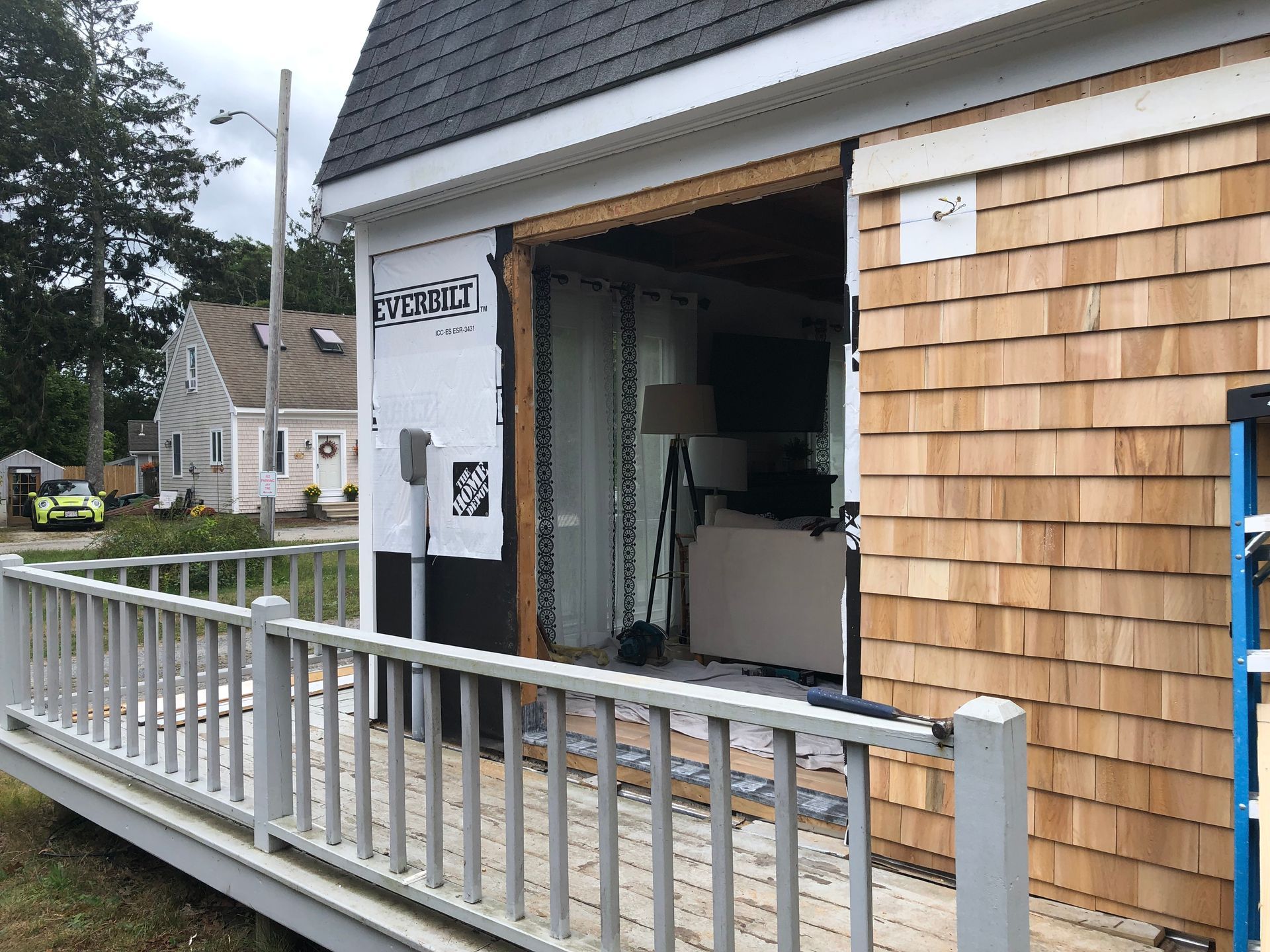 Exterior of a house under construction; open sliding door, cedar shingles, and deck with a railing.