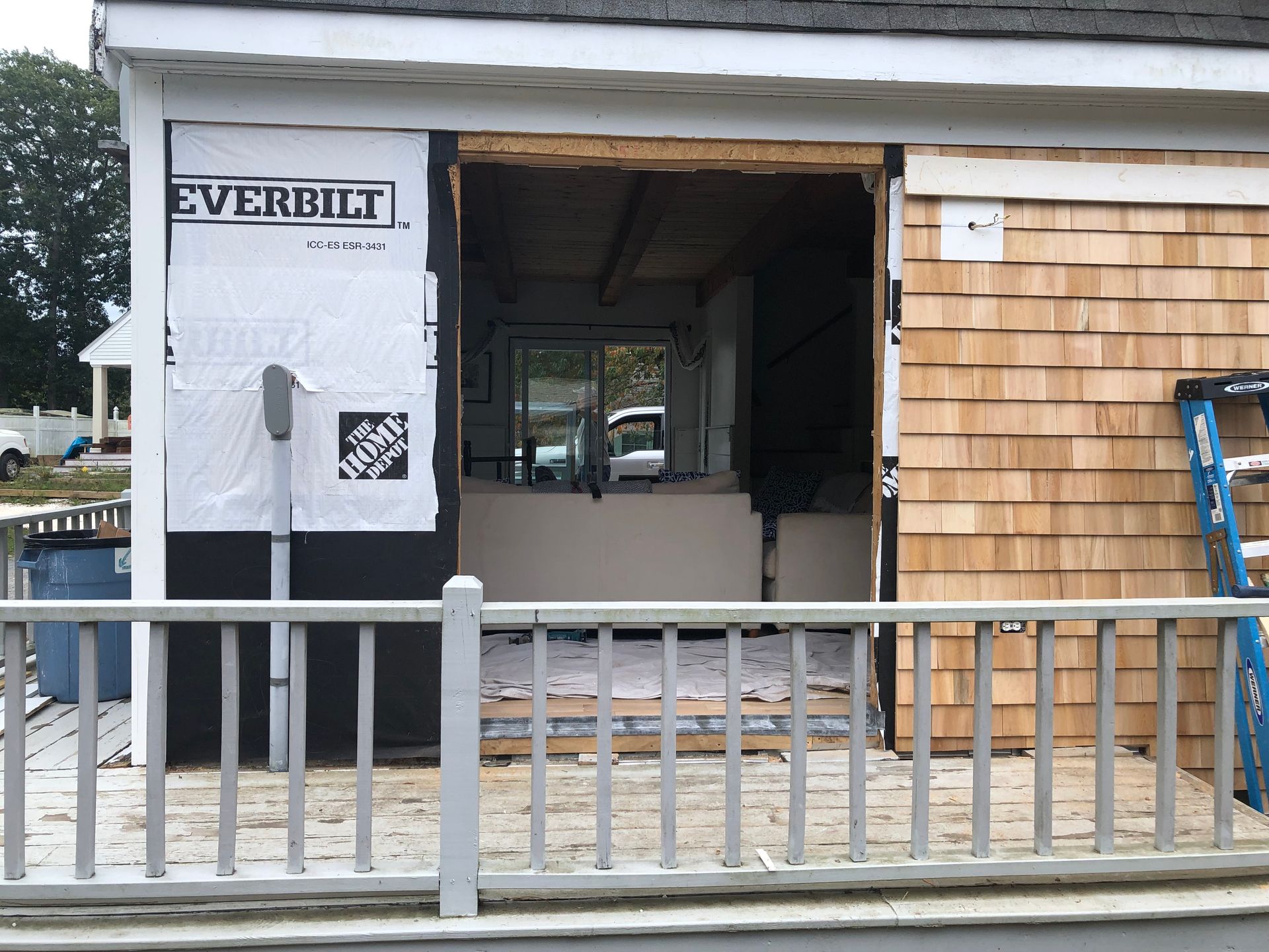 Exterior of a building under construction. Opening for a window or door. Deck with railing in the foreground.