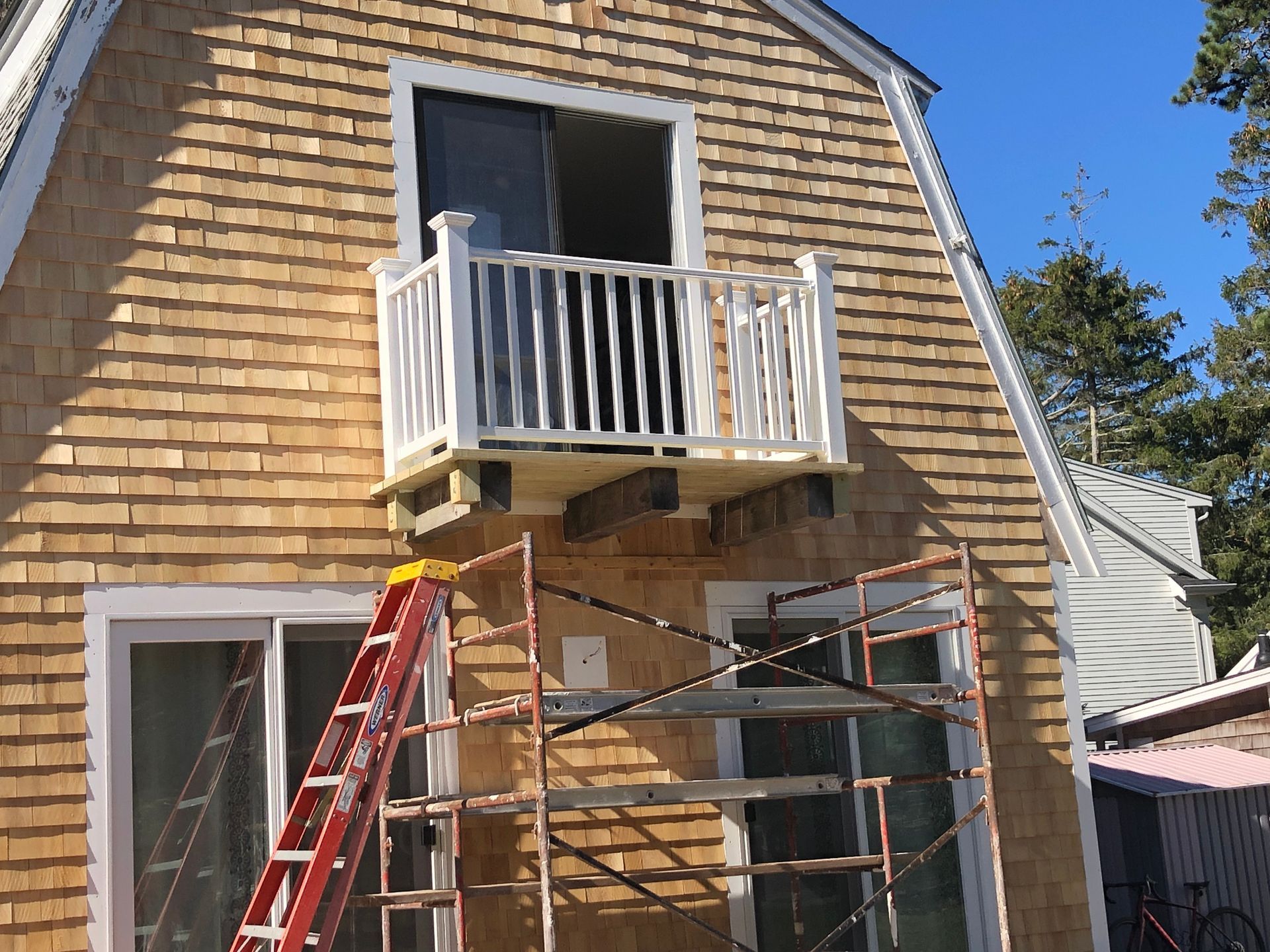 House exterior with newly built white balcony, cedar shingle siding, scaffolding, and a ladder.