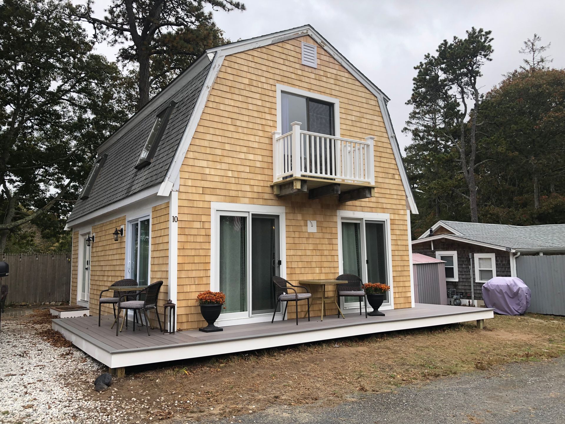 A light-yellow Dutch-style house with a balcony and deck, trees in the background.