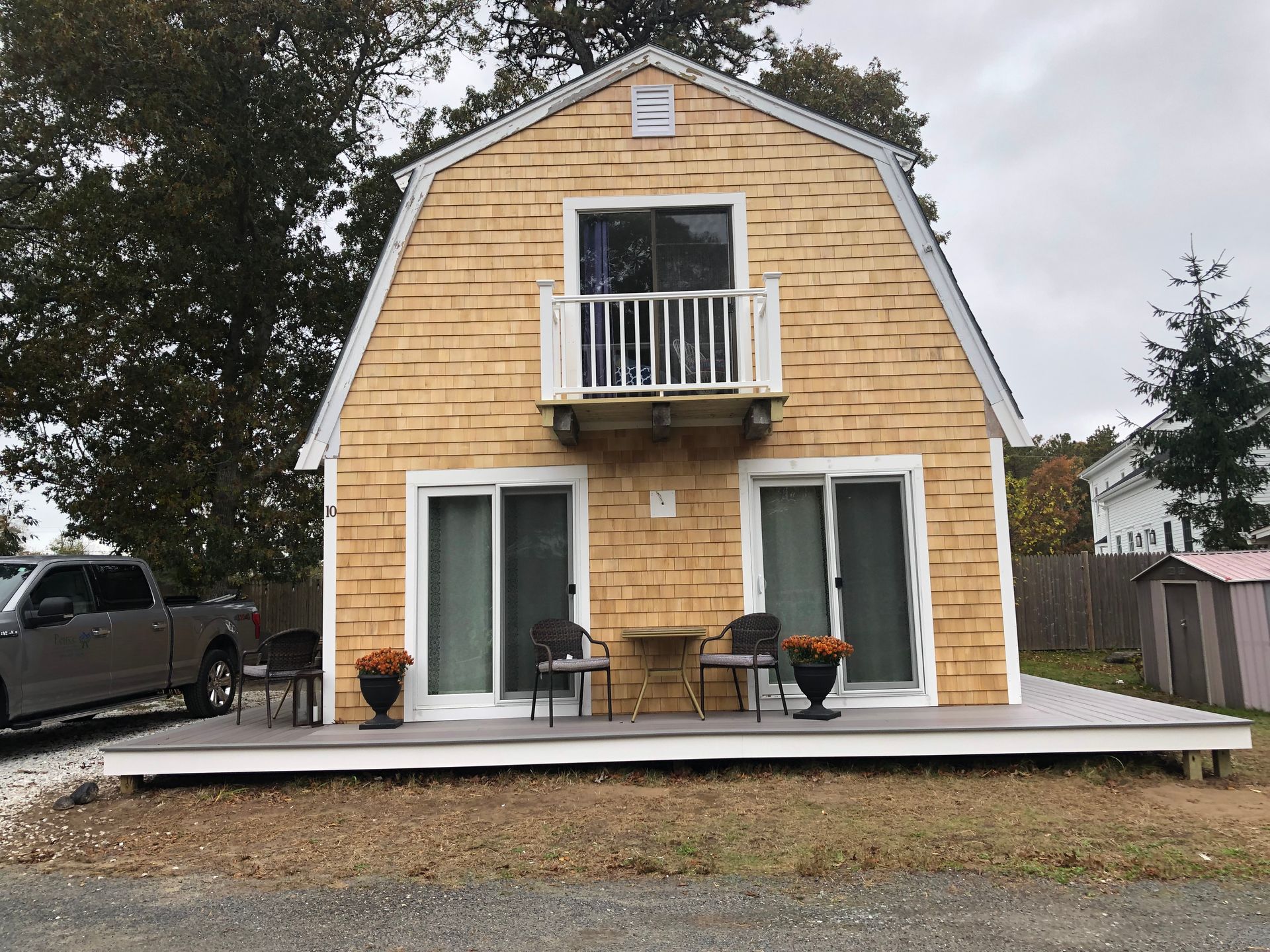 Yellow-sided barn-style building with a deck, balcony, and sliding glass doors. A pickup truck is parked to the left.